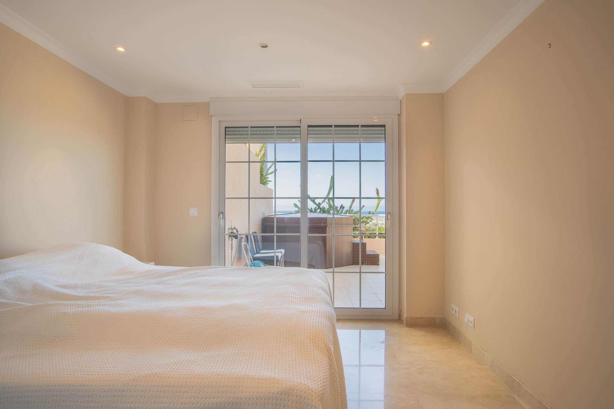 Bright bedroom featuring marble flooring and sliding glass doors that open onto a private terrace with a jacuzzi and sea views.