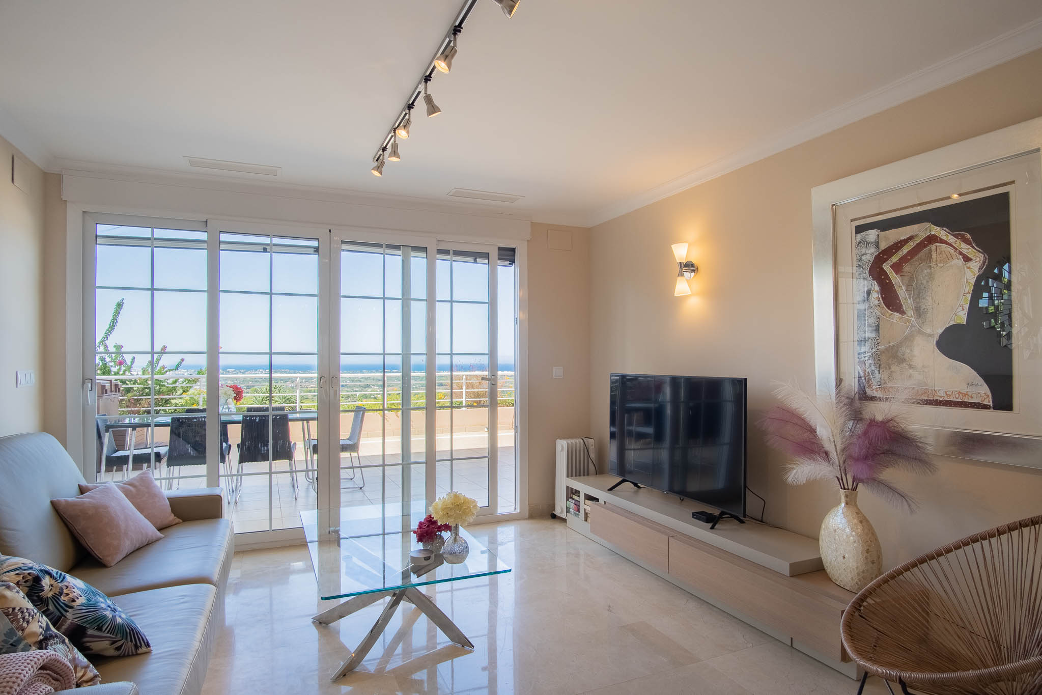 Bright living area featuring polished marble floors, contemporary furniture, and large sliding doors opening to a terrace with expansive coastal views.