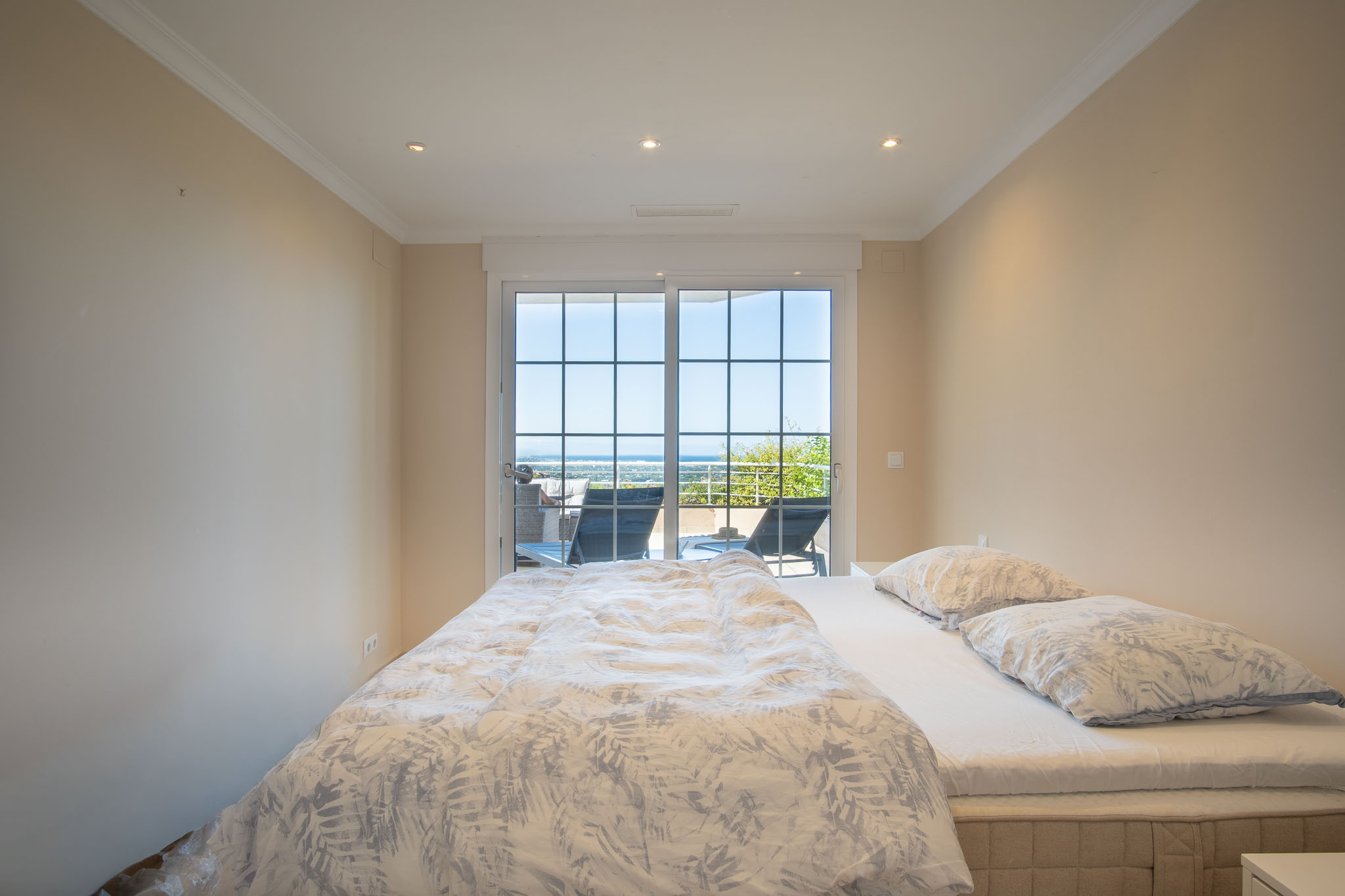 Double bedroom featuring direct terrace access through grid-patterned sliding doors, offering panoramic sea views and recessed ceiling lighting.