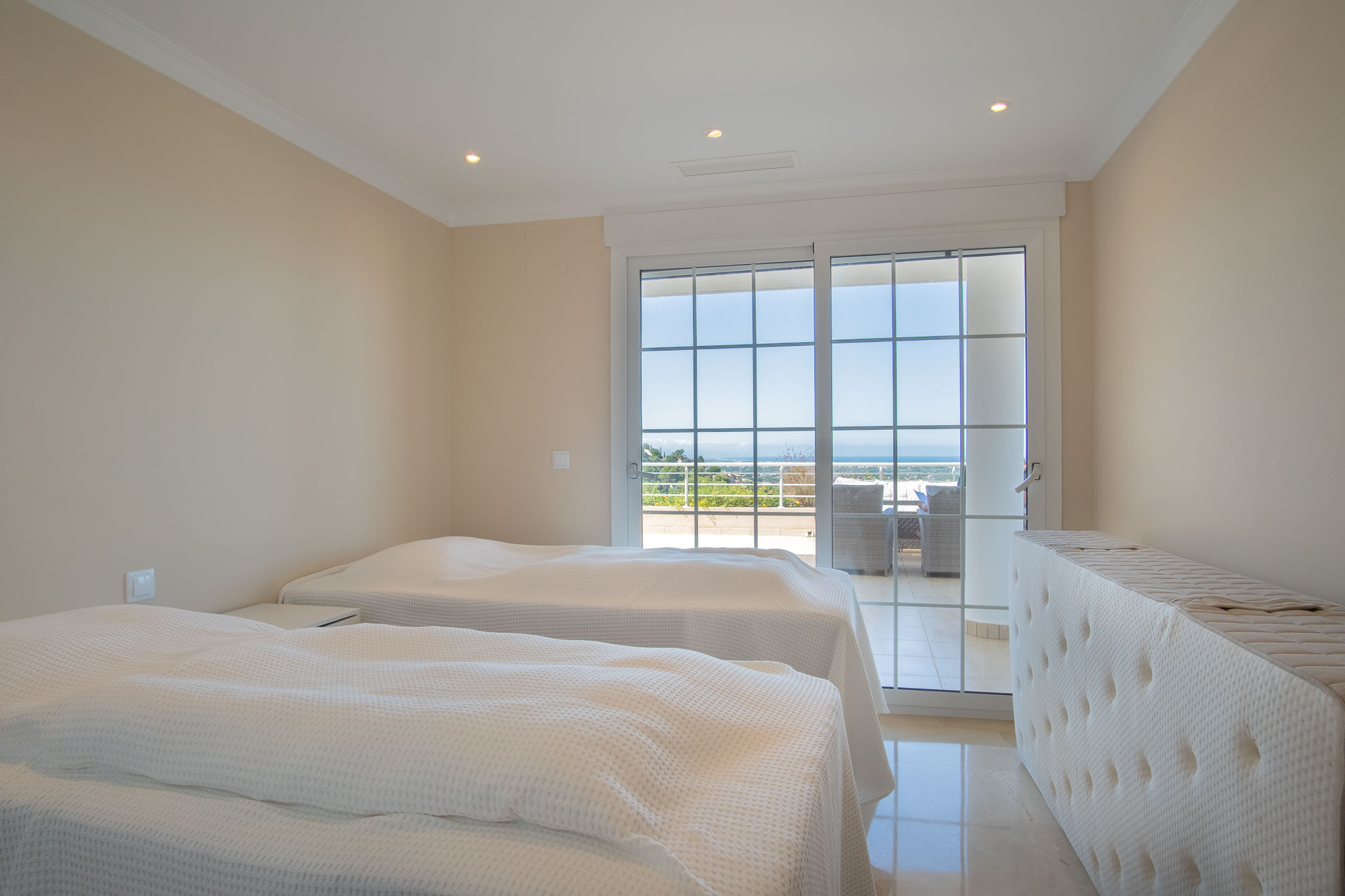 Double bedroom featuring polished marble floors and sliding glass doors with muntins that open onto a terrace with Mediterranean views.
