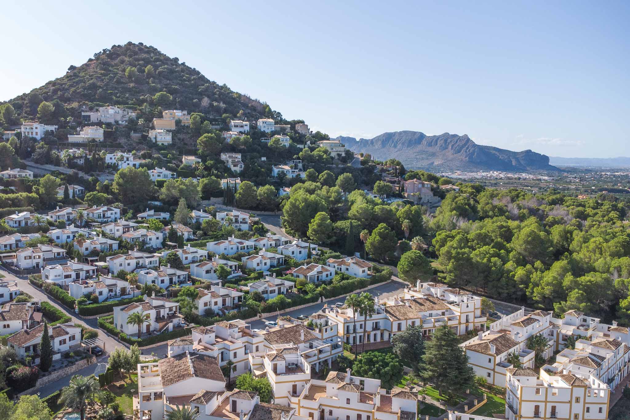 Elevated panoramic view of the La Sella residential area, showcasing Mediterranean-style architecture integrated into a lush pine hillside with mountain vistas.