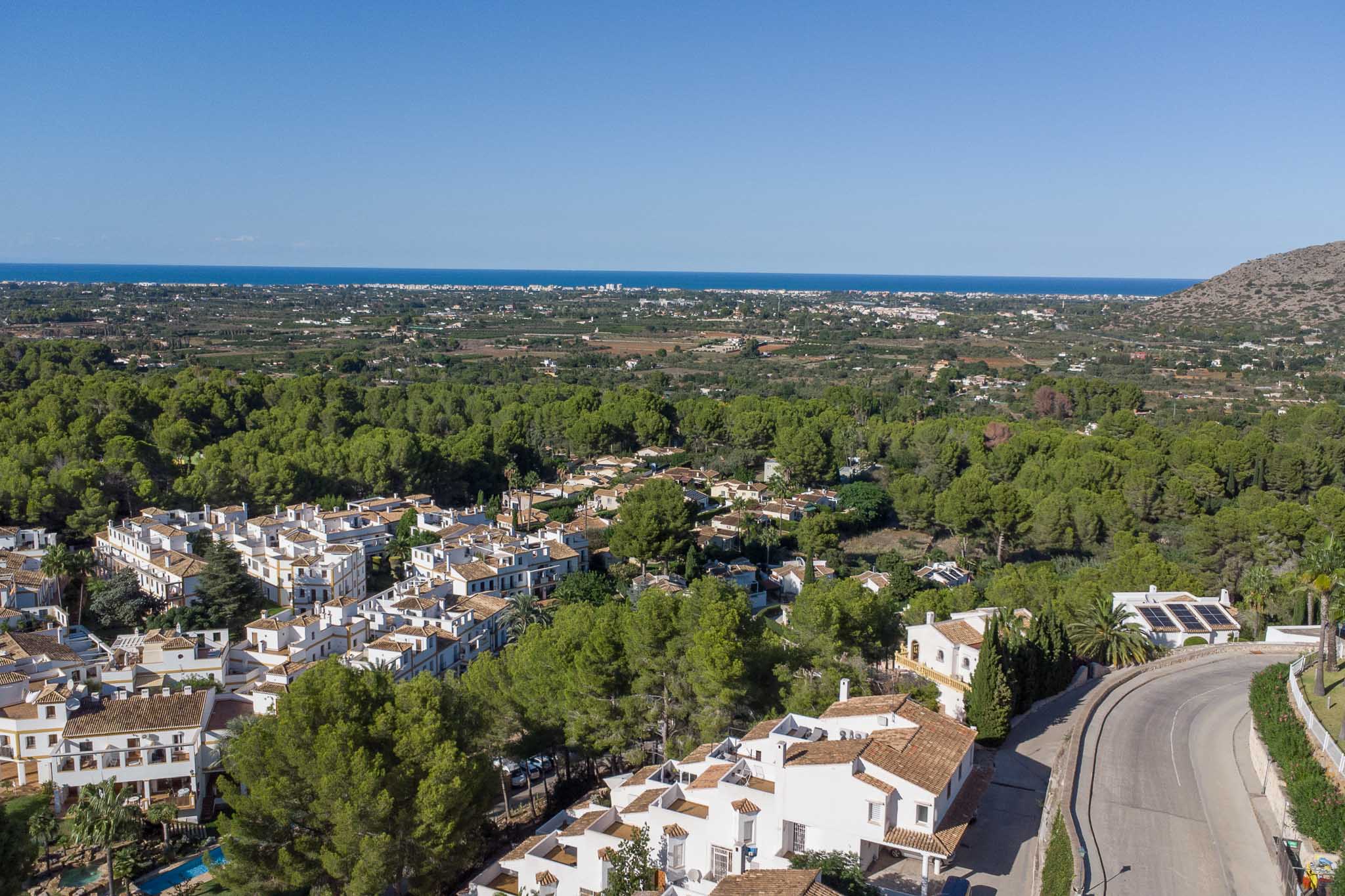 Elevated panoramic view of the Las Mimosas residential complex, nestled within a pine forest with clear views of the Mediterranean coastline.