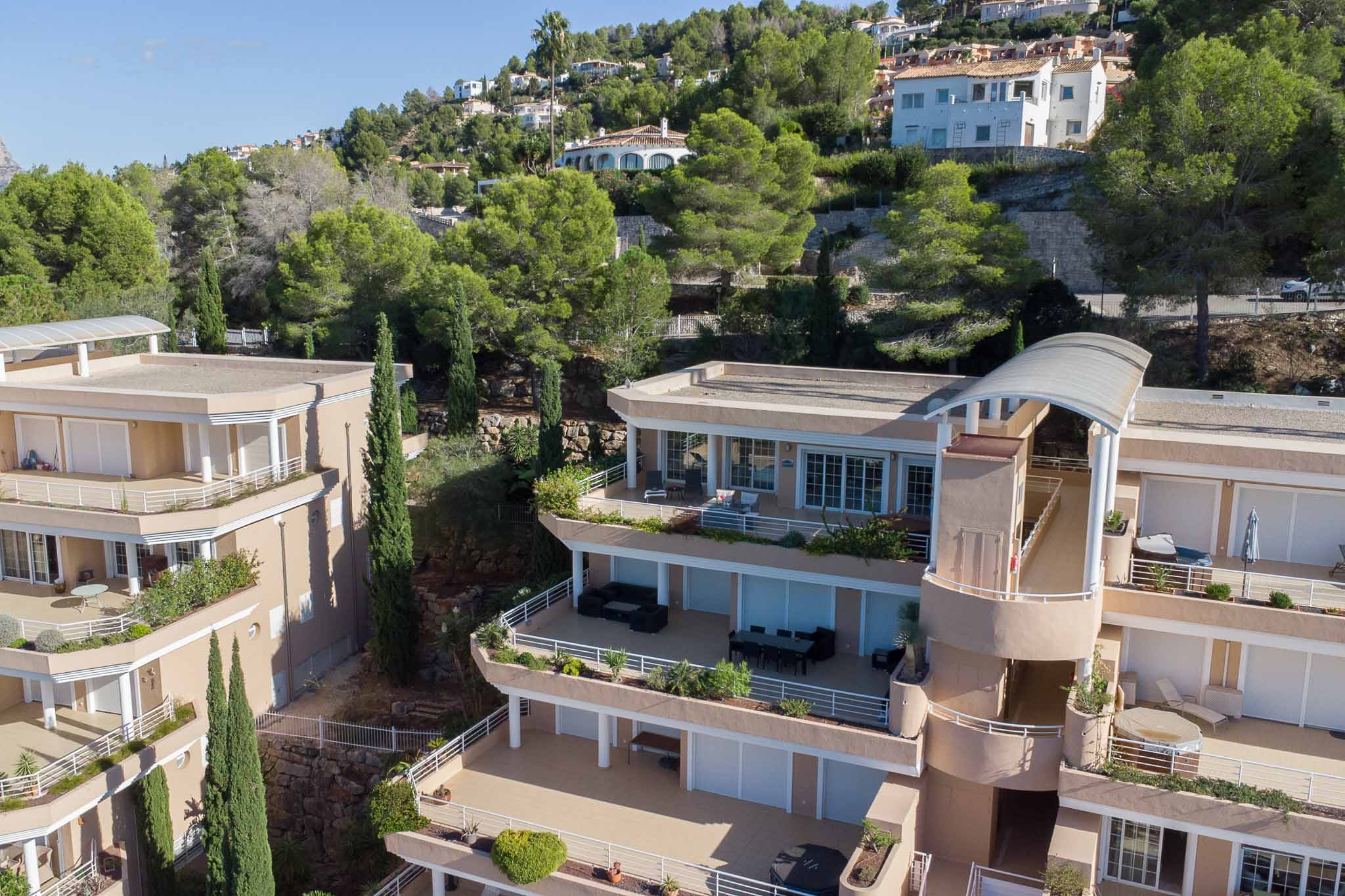 Exterior view of Las Mimosas complex, showcasing tiered architecture with expansive private terraces and earth-toned facades integrated into the wooded hillside of La Sella.