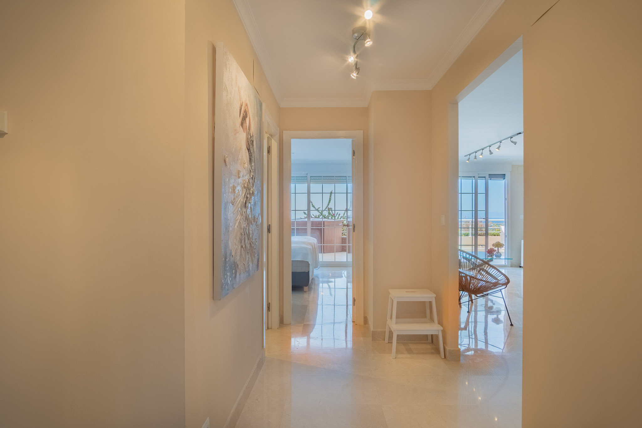 Hallway featuring polished marble flooring and track lighting, providing access to the living area and a bedroom with views of the Mediterranean.