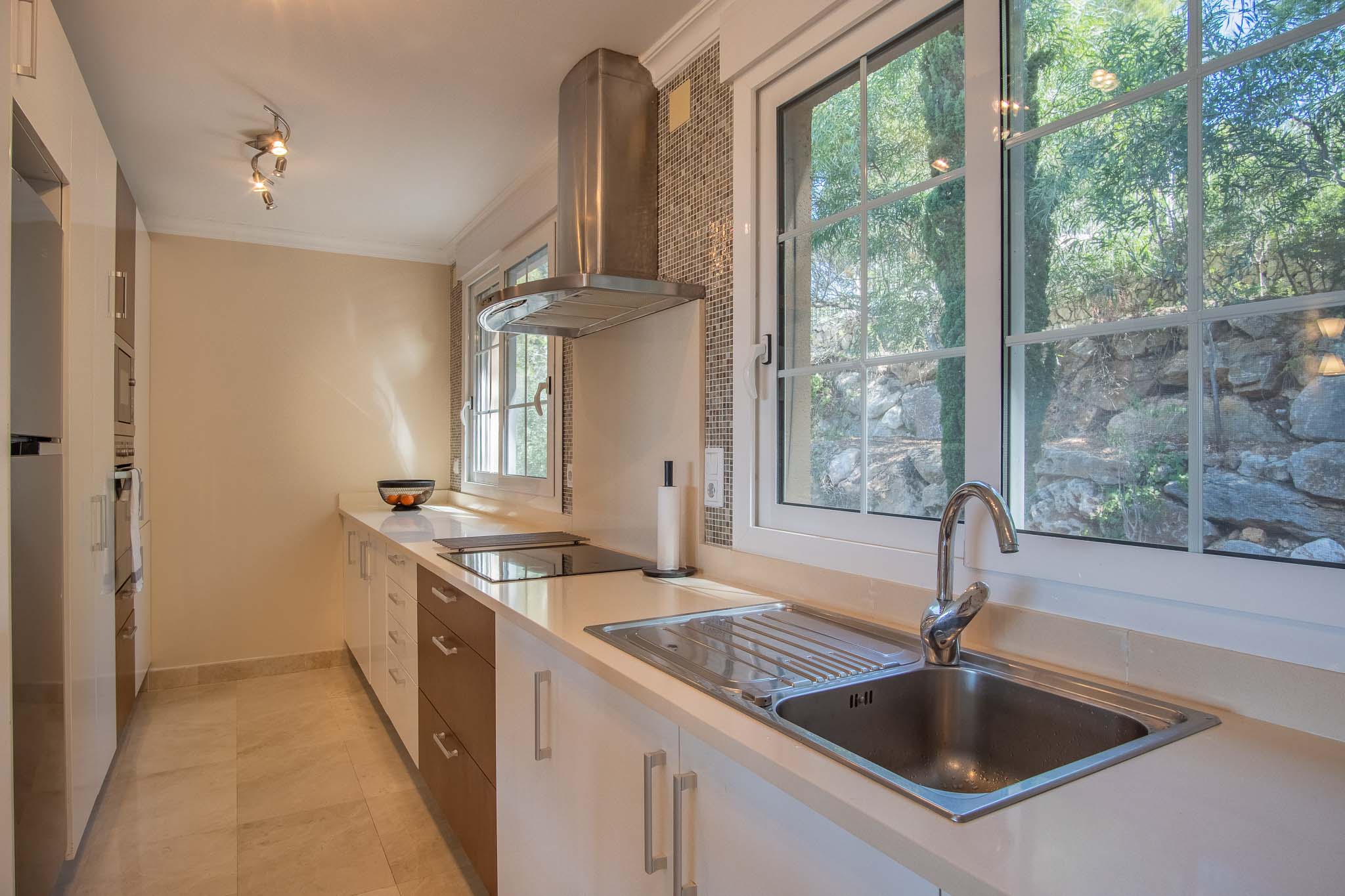 Modern kitchen featuring white countertops, stainless steel extractor, and large windows overlooking the landscaped garden and rockery.