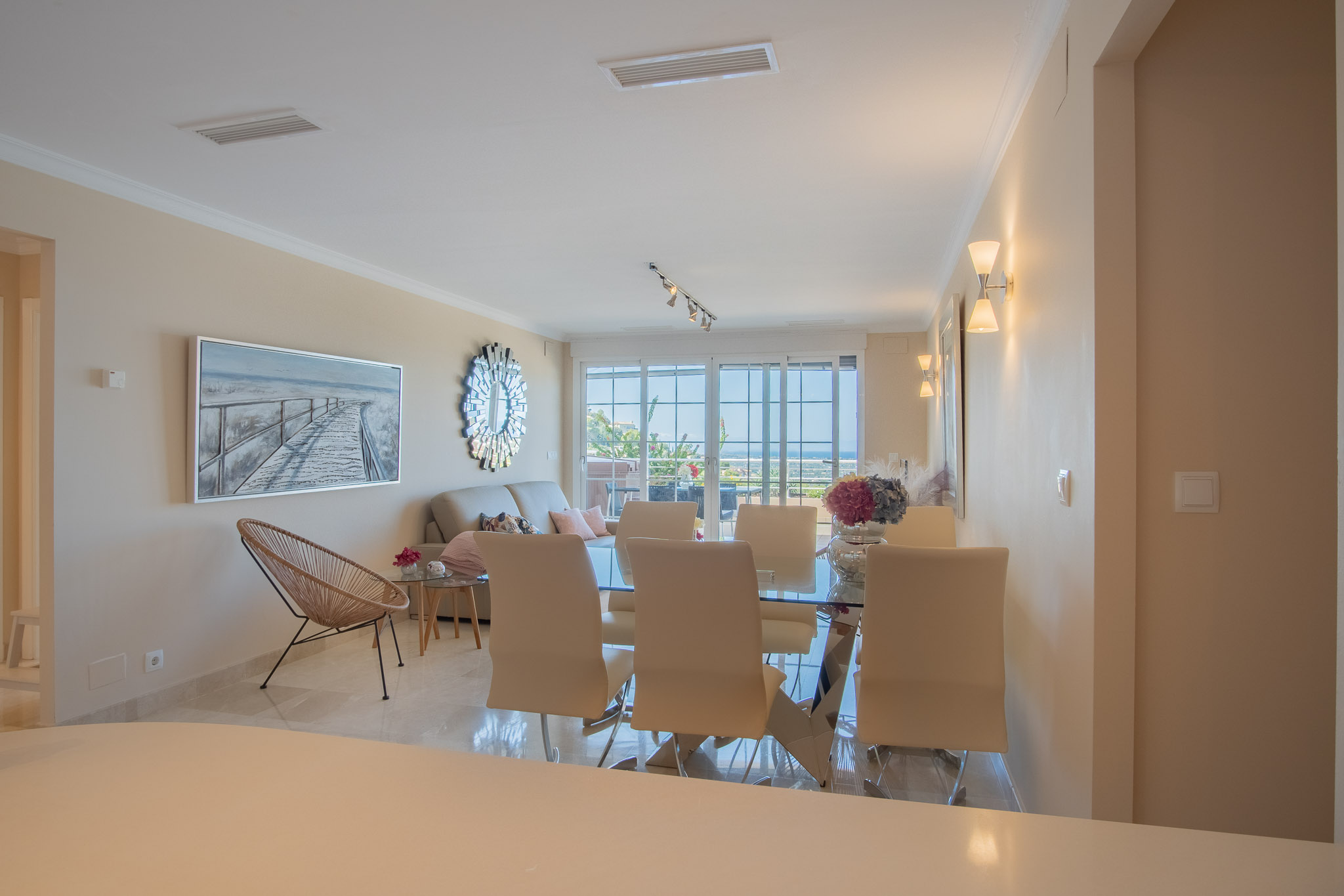 Open-plan living and dining area featuring polished marble floors, a glass dining table, and large sliding doors opening to a terrace with sea views.