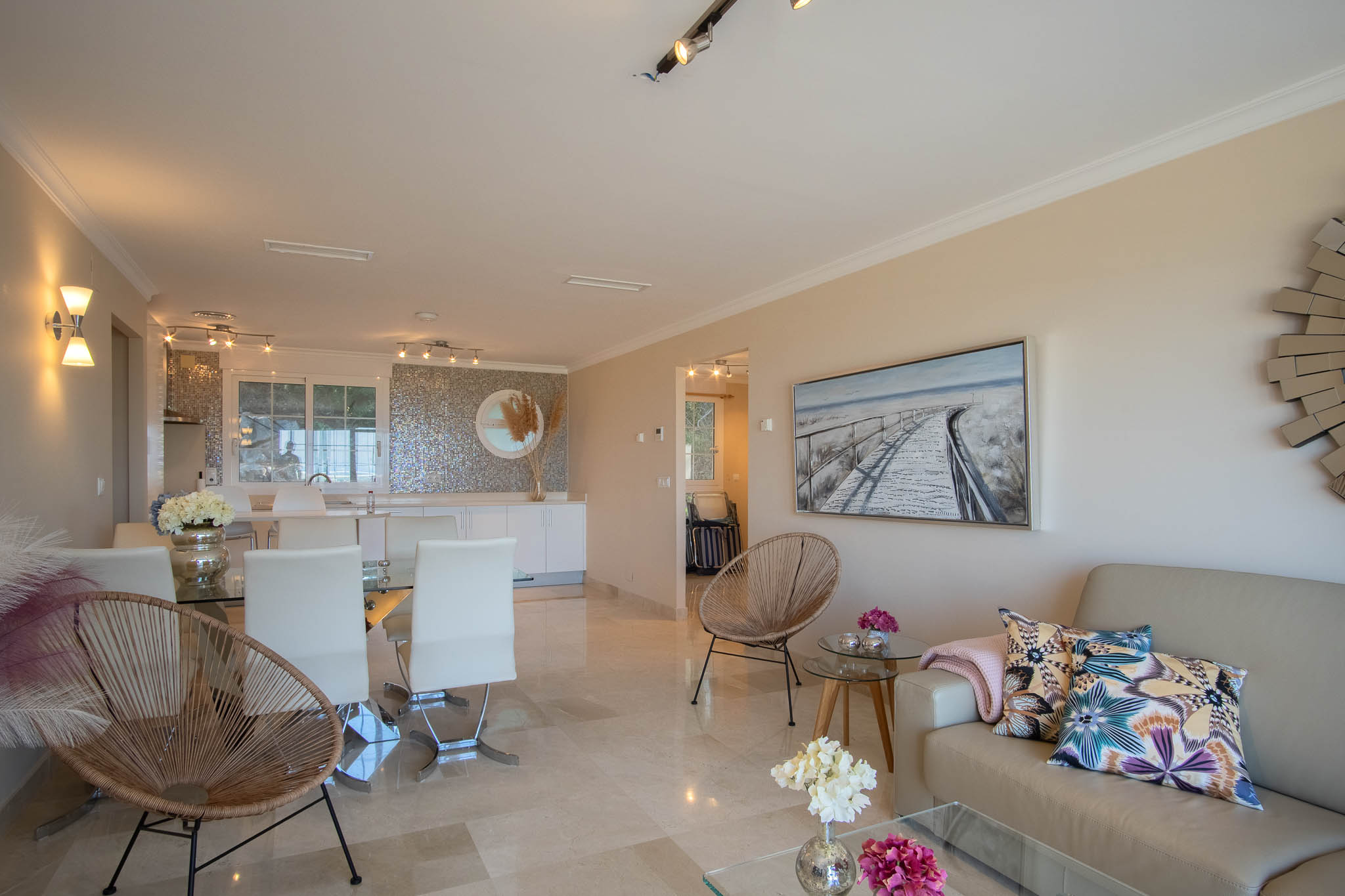 Open-plan living and dining area featuring polished marble floors, contemporary furniture, and a modern kitchen with a unique iridescent mosaic backsplash.