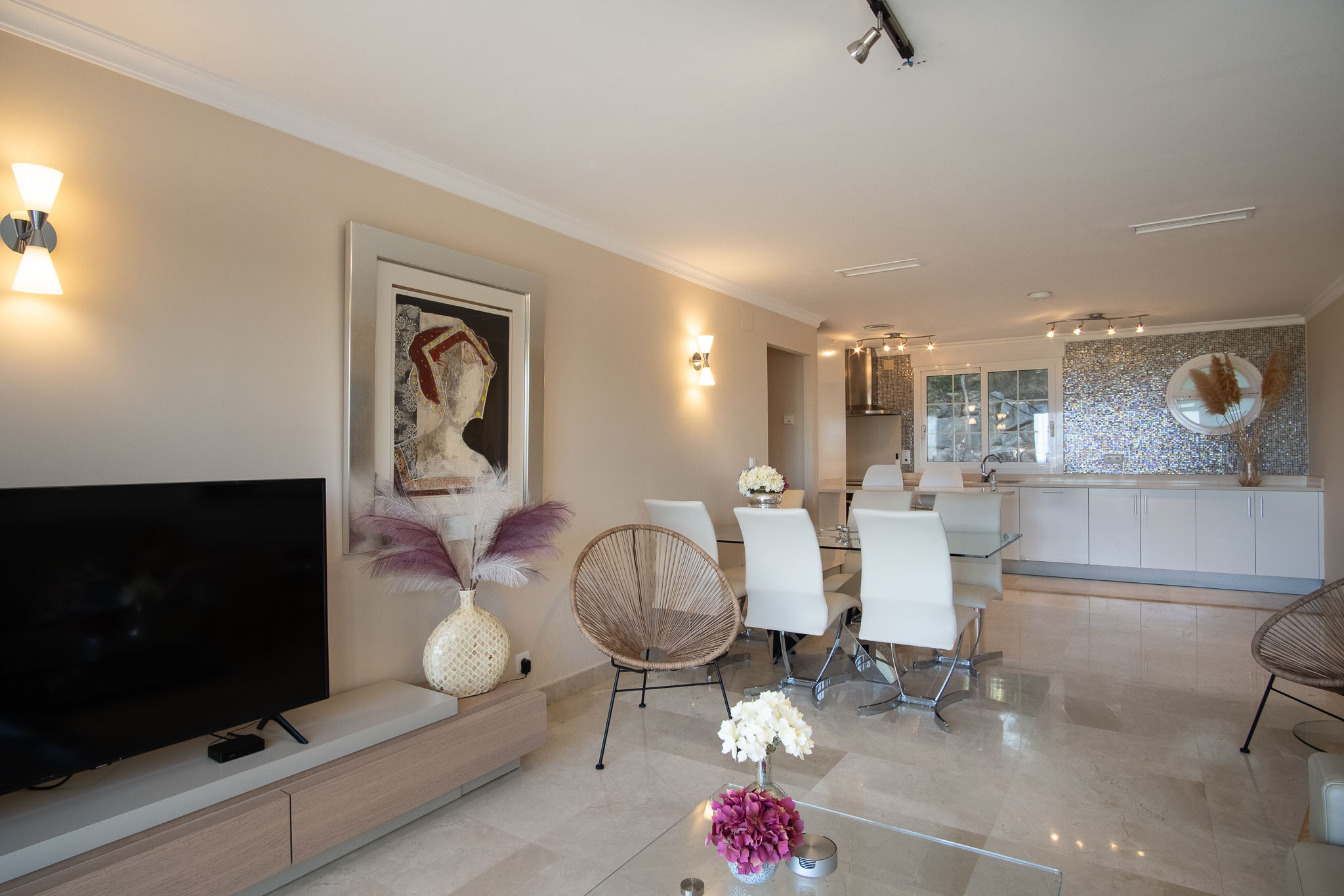Open-plan living and dining area featuring polished marble floors, modern furniture, and an integrated kitchen with a unique iridescent mosaic backsplash.