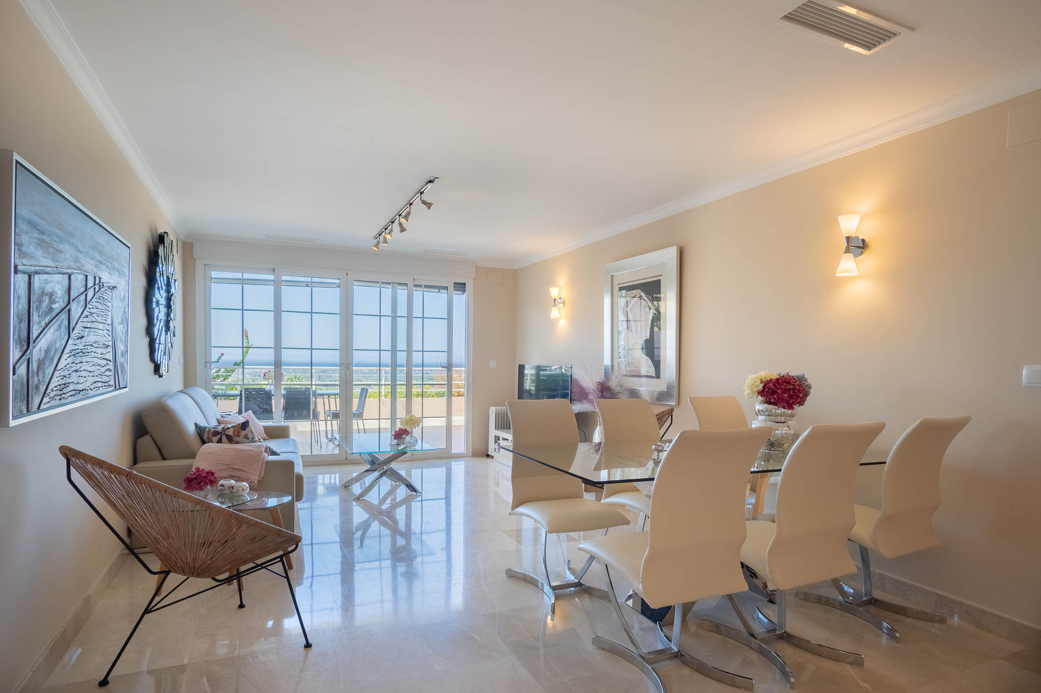 Open-plan living and dining area featuring polished marble floors, modern glass furniture, and large sliding doors opening to a terrace with Mediterranean views.