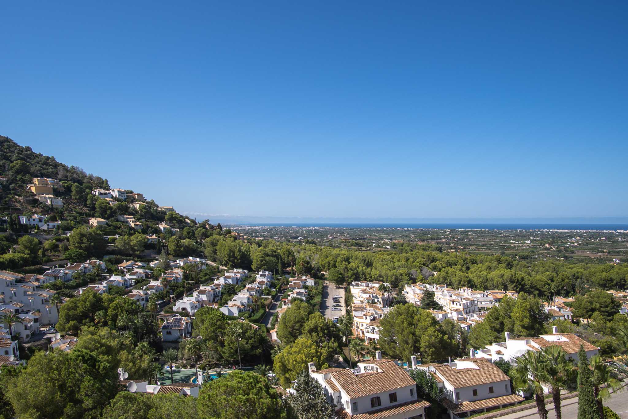 Panoramic views from La Sella towards the Mediterranean Sea, showcasing residential architecture integrated into lush green surroundings under clear skies.