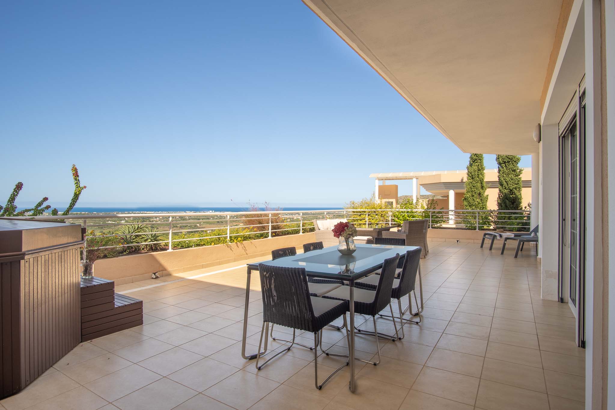 Spacious terrace featuring a private wood-paneled jacuzzi, outdoor dining set, and panoramic Mediterranean Sea views. The area is finished with ceramic tiling and white railings.