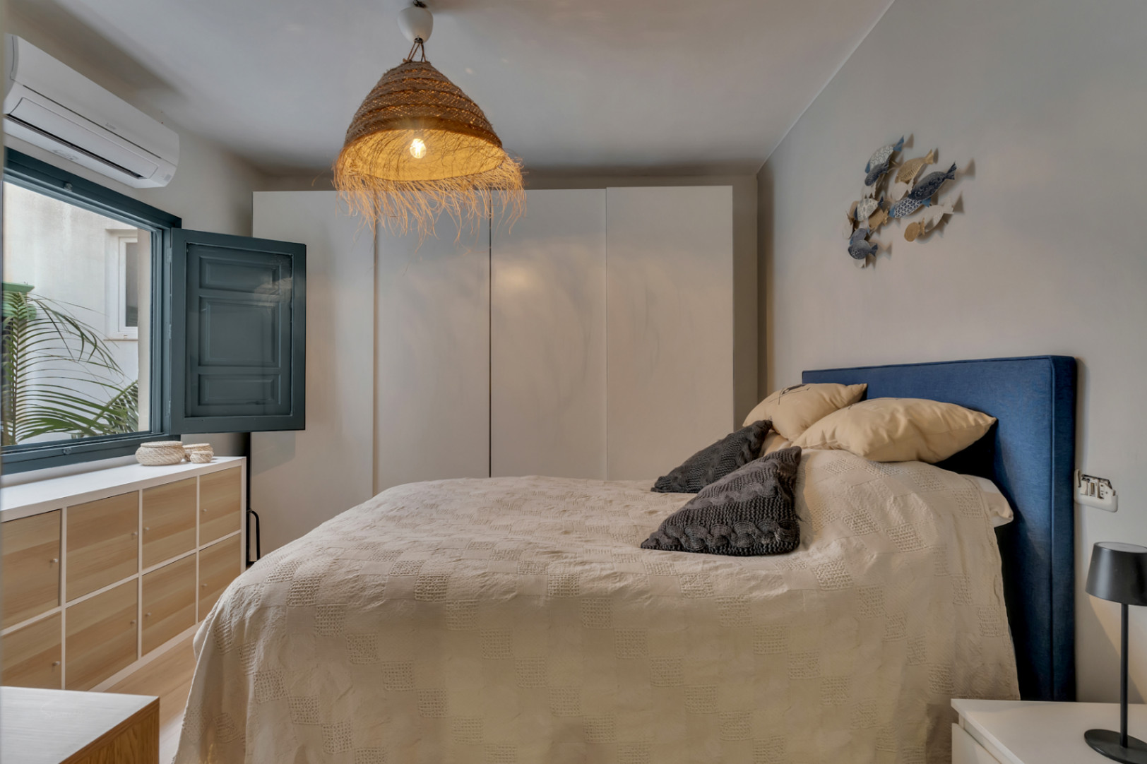 Bright bedroom featuring a blue headboard, wicker lamp, and a window with shutters.
