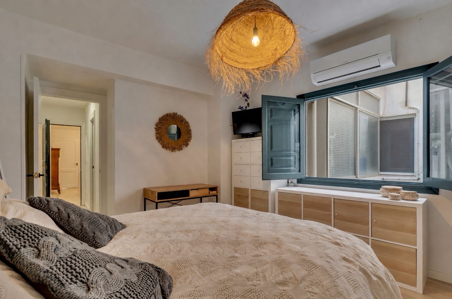 Bright bedroom with double bed, blue wood window frame, and a hanging wicker lamp.
