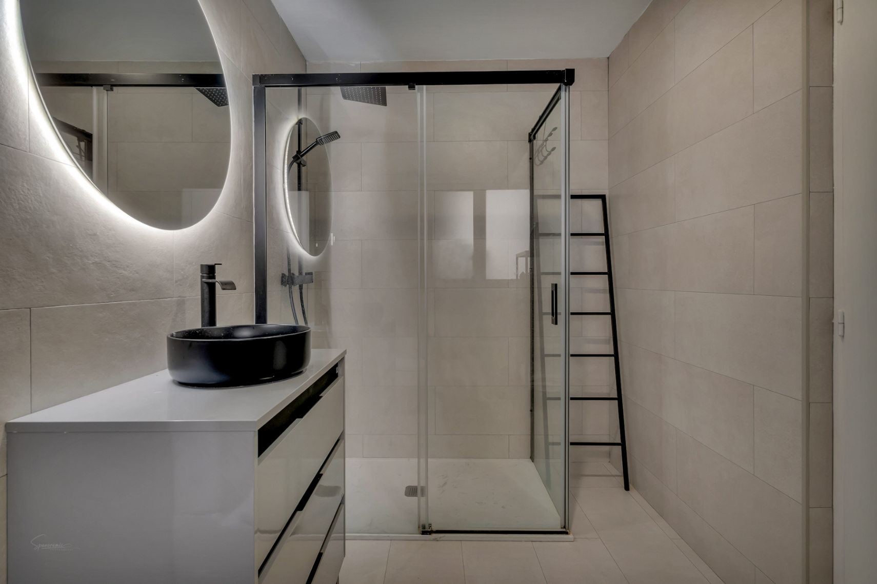 Detail of the modern bathroom with a black sink on a white countertop and glass-enclosed shower.