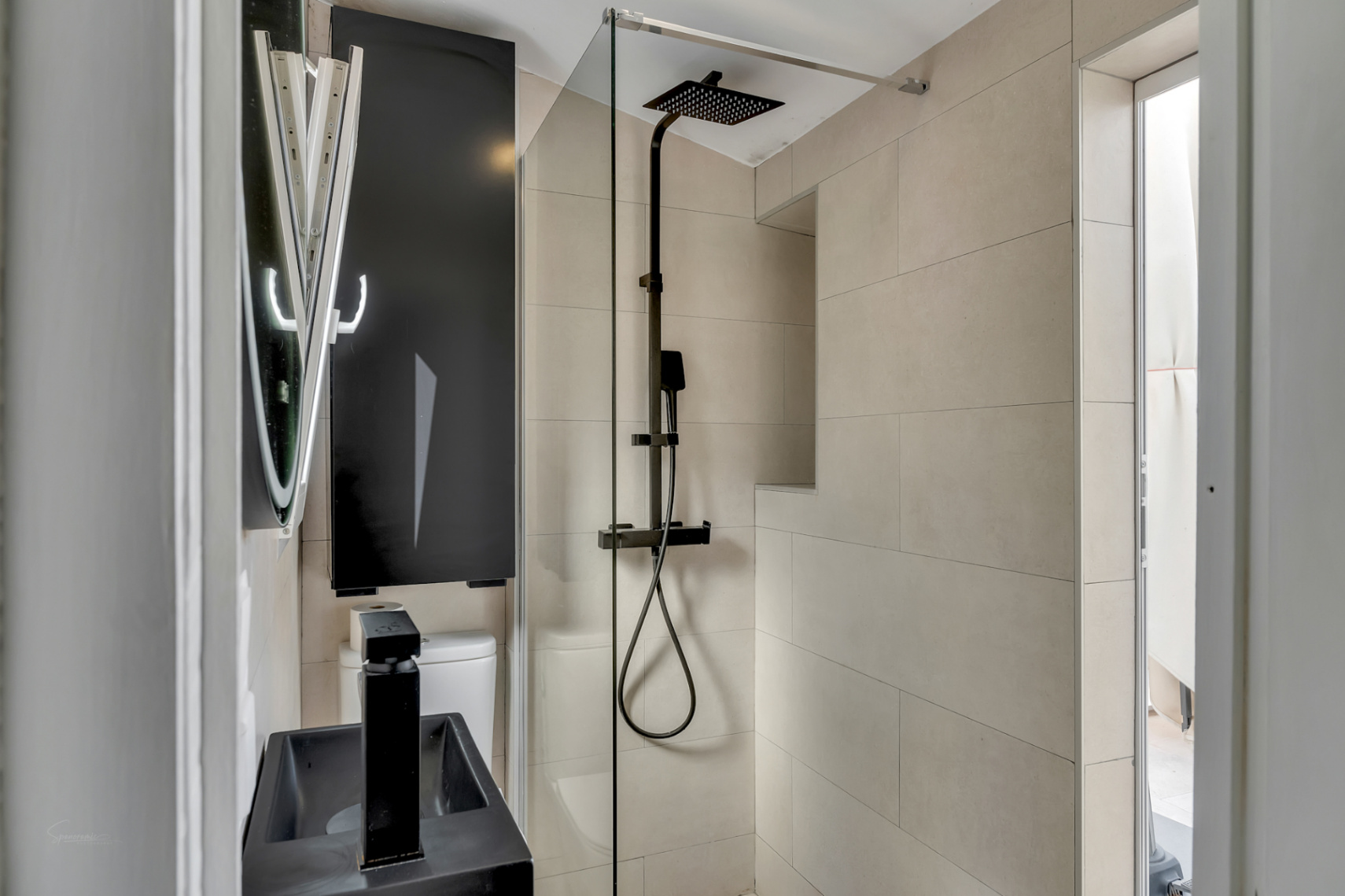 Detail of the modern bathroom with black rainfall shower, black sink, and cream-colored tiles.