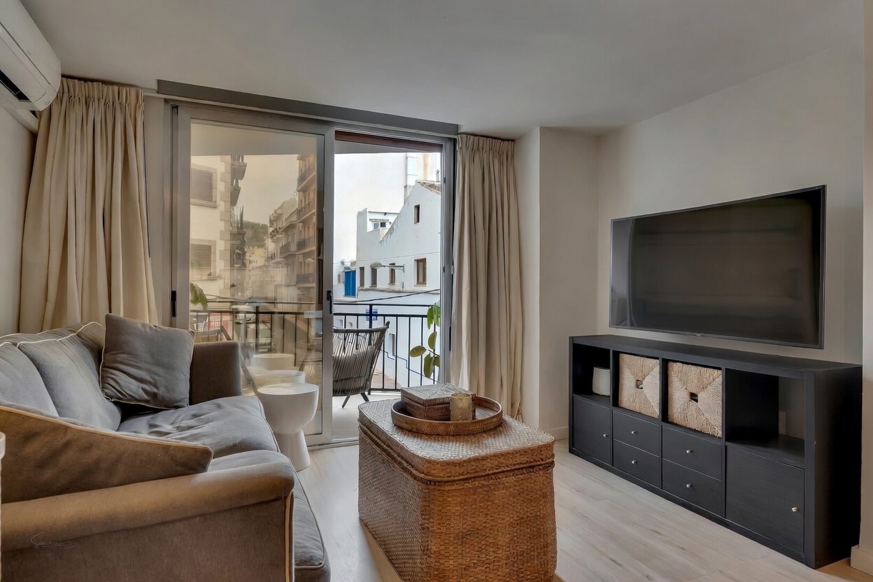 Modern living room featuring a gray sofa, black TV stand, and balcony access with urban views.