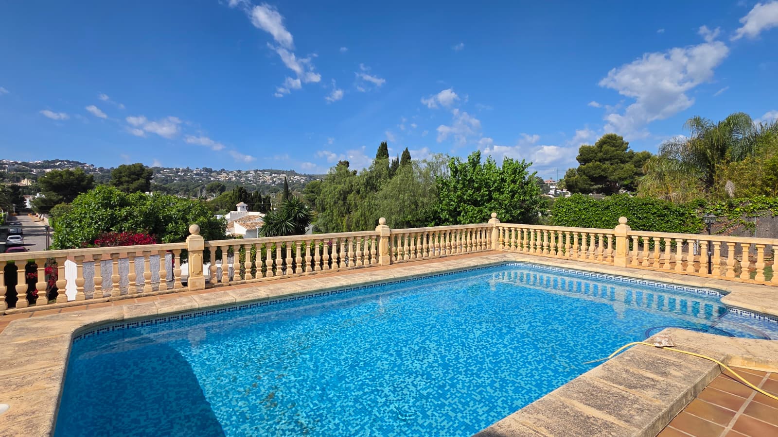 Elevated swimming pool with blue mosaic tiling, bordered by a traditional stone balustrade and offering panoramic views of the Jávea landscape.