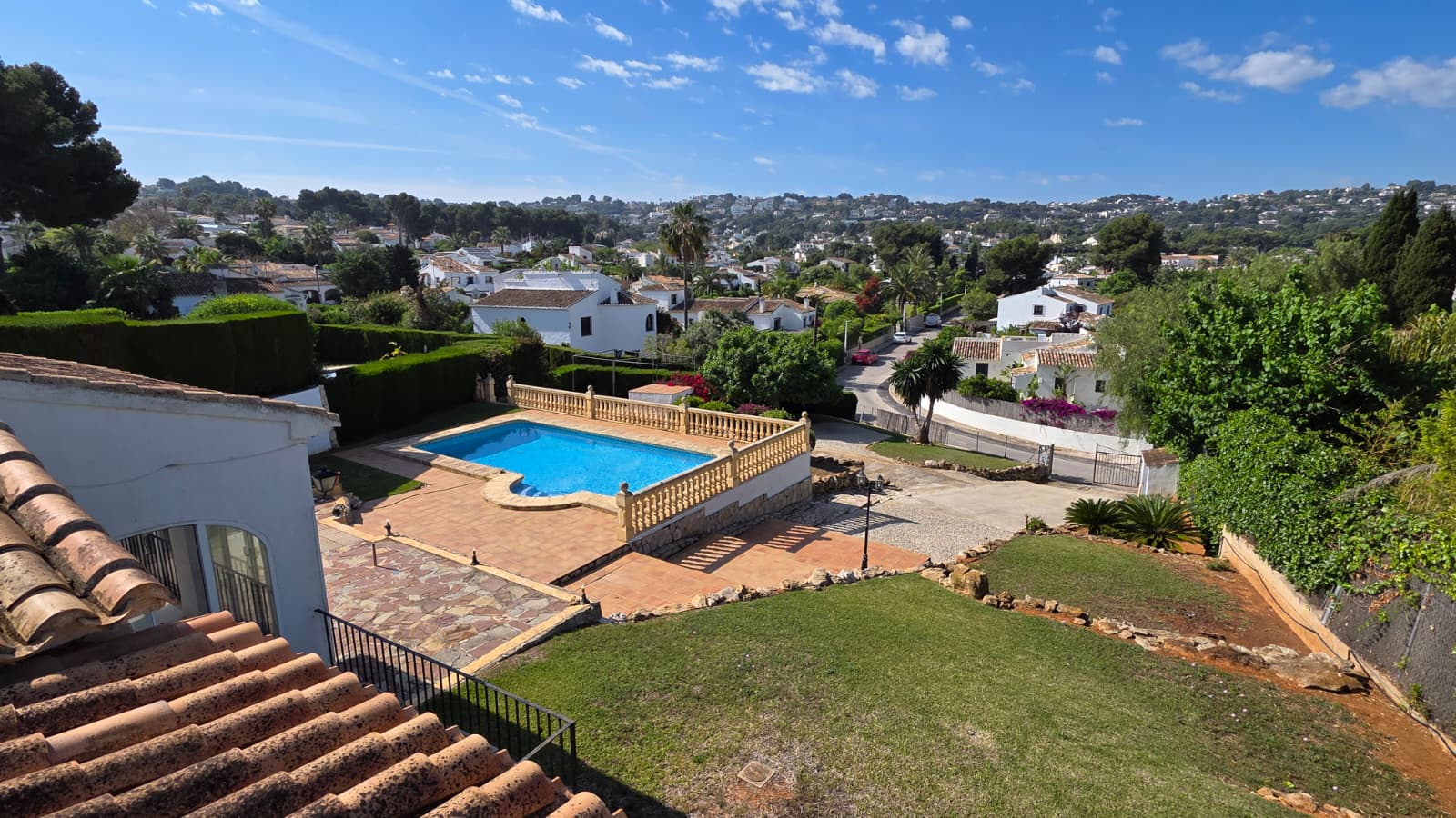 Elevated view of the private pool area with stone balustrades, terracotta terrace, and lawn, overlooking the El Tosalet urbanization in Jávea.