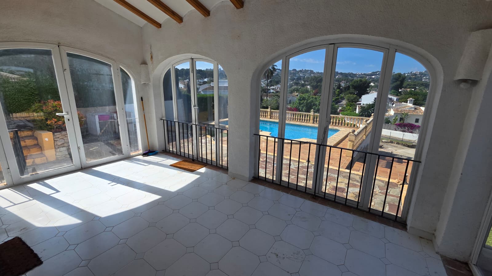 Enclosed naya featuring arched windows, white tiled flooring, and exposed wooden beams, overlooking the private swimming pool and Jávea hillside.