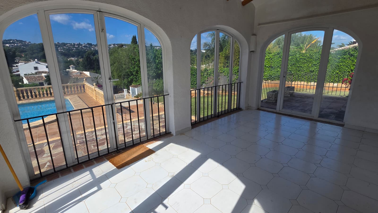 Glazed naya featuring white tiled flooring and arched windows providing views over the private swimming pool and Mediterranean garden.