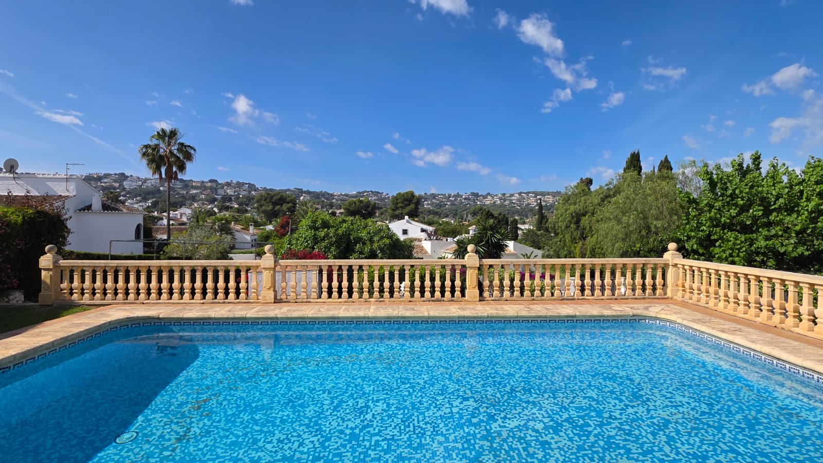 Outdoor swimming pool with blue mosaic tiling and a classic stone balustrade, featuring panoramic views over the surrounding hills and Jávea landscape.