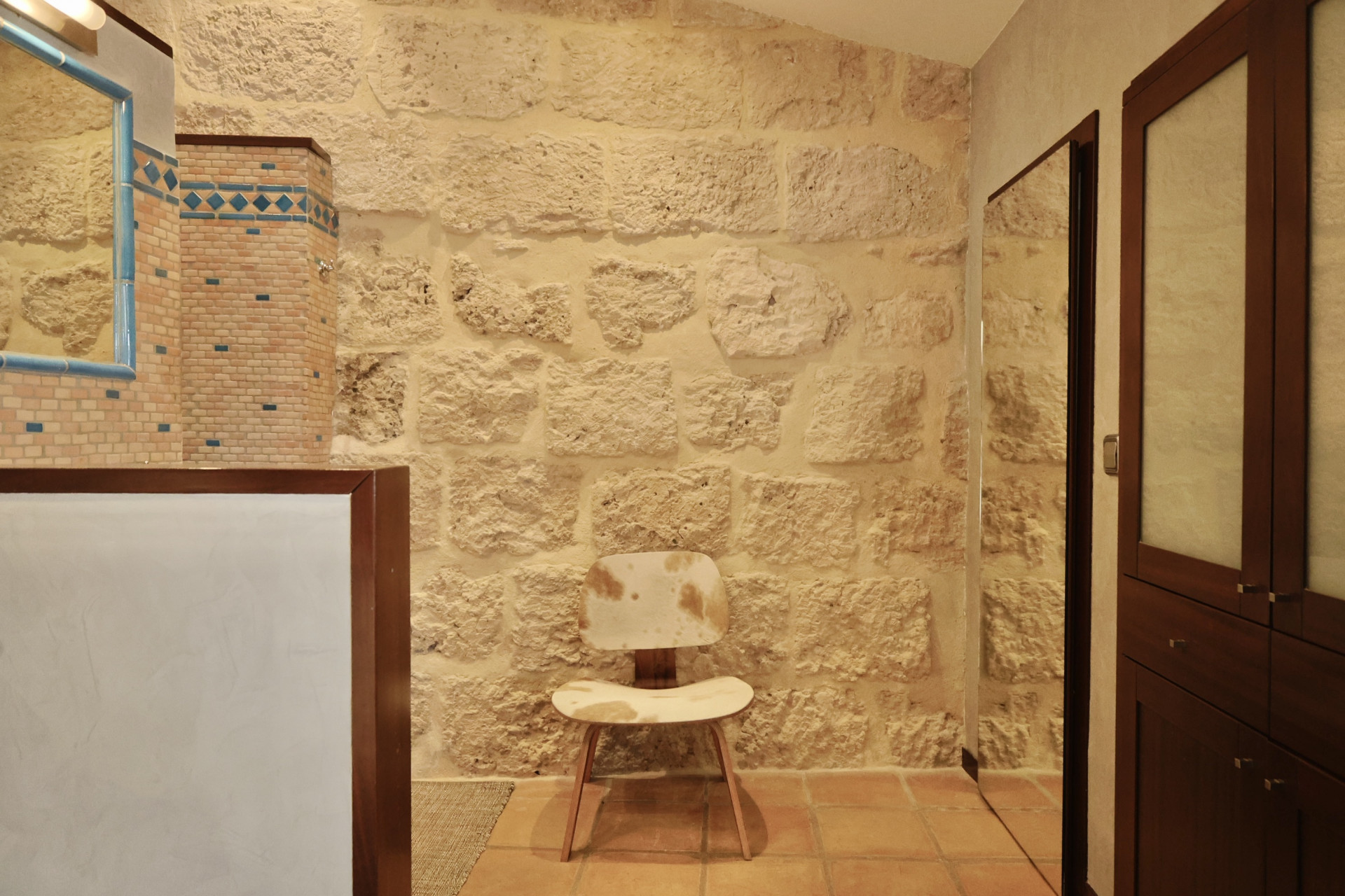 Bathroom detail featuring a rustic stone wall, blue-framed mirror, and a designer chair with cowhide upholstery.