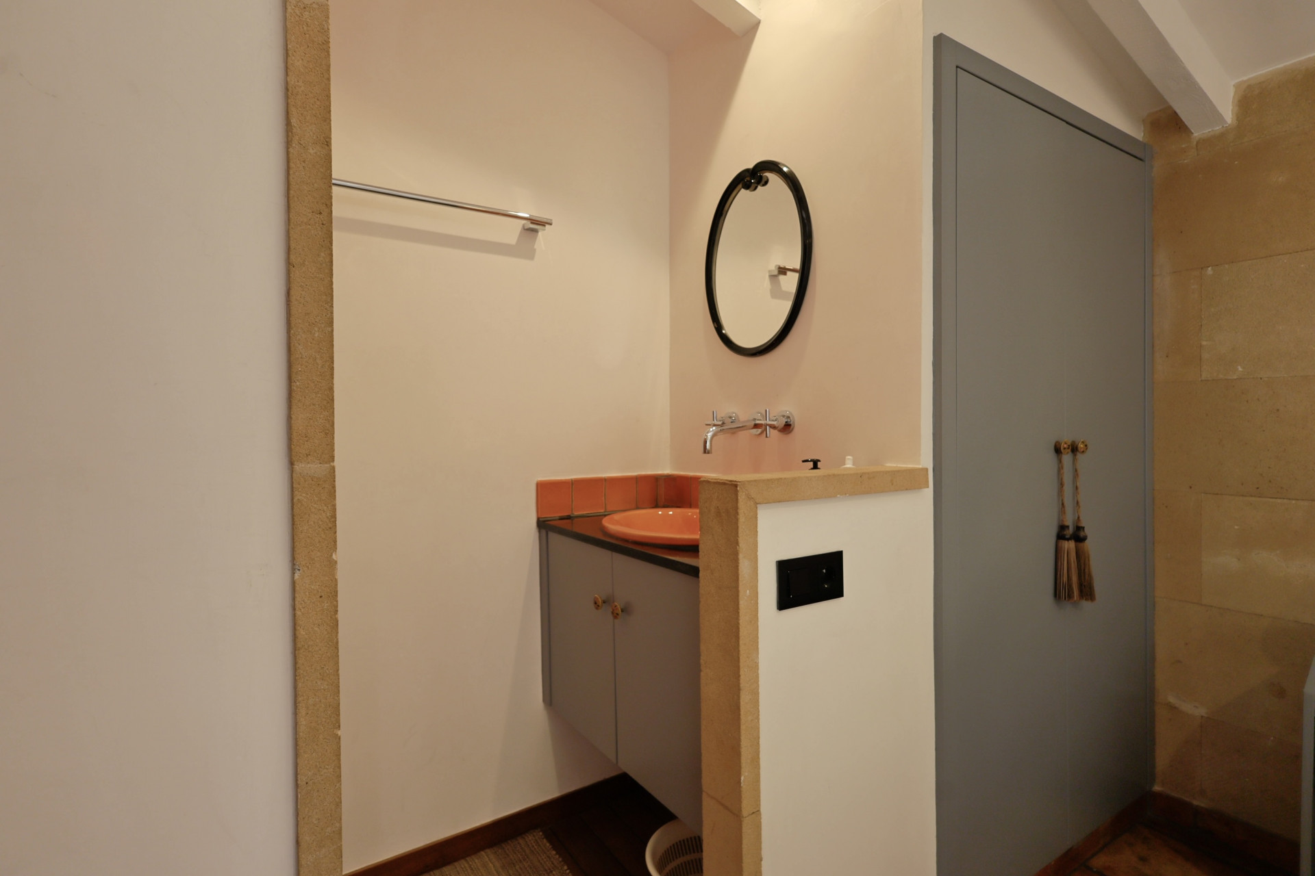 Bathroom detail featuring an orange ceramic sink, oval mirror, and a gray door with decorative tassels.