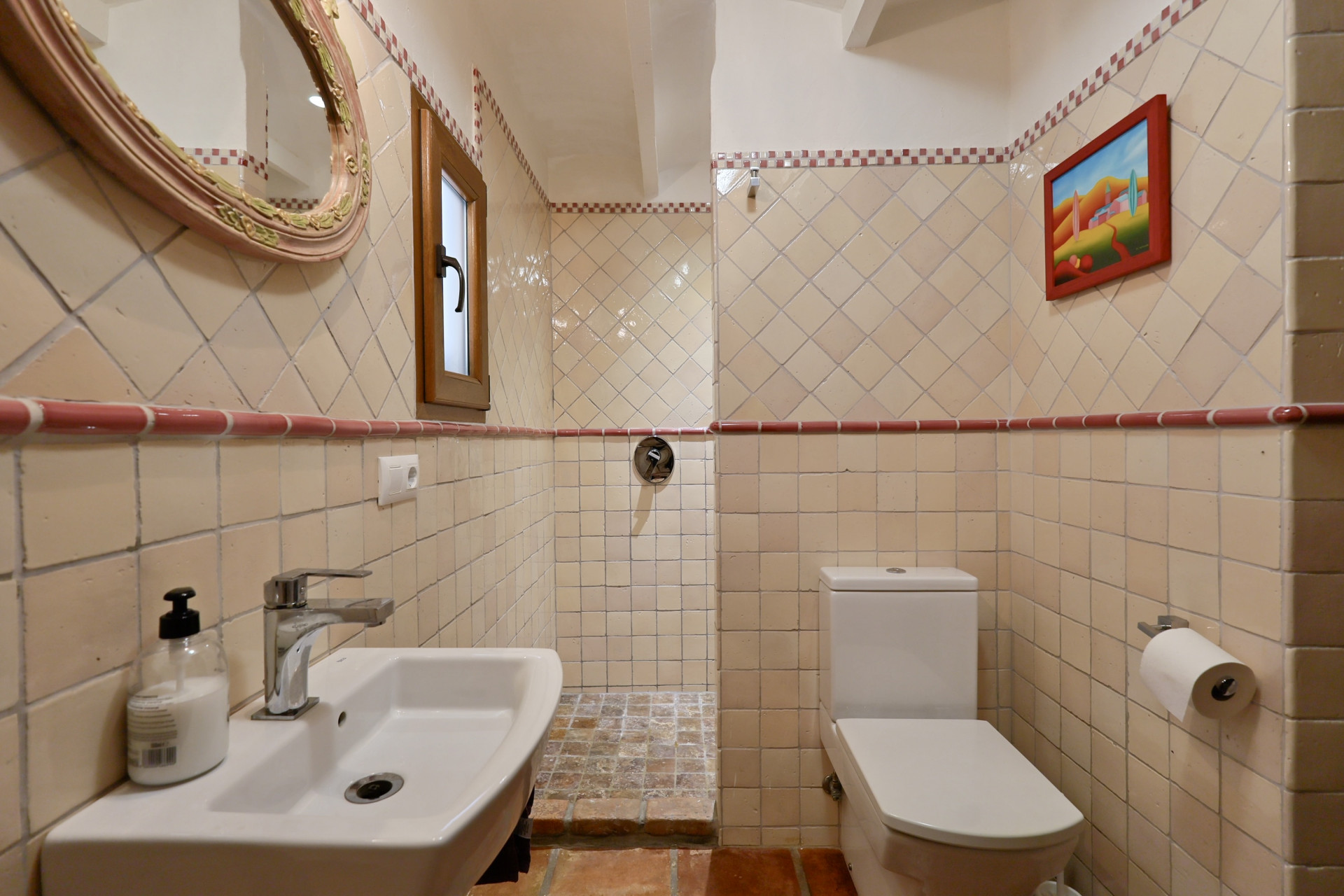 Bathroom detail with cream tiles, oval mirror, and white sink in Jávea Villa.