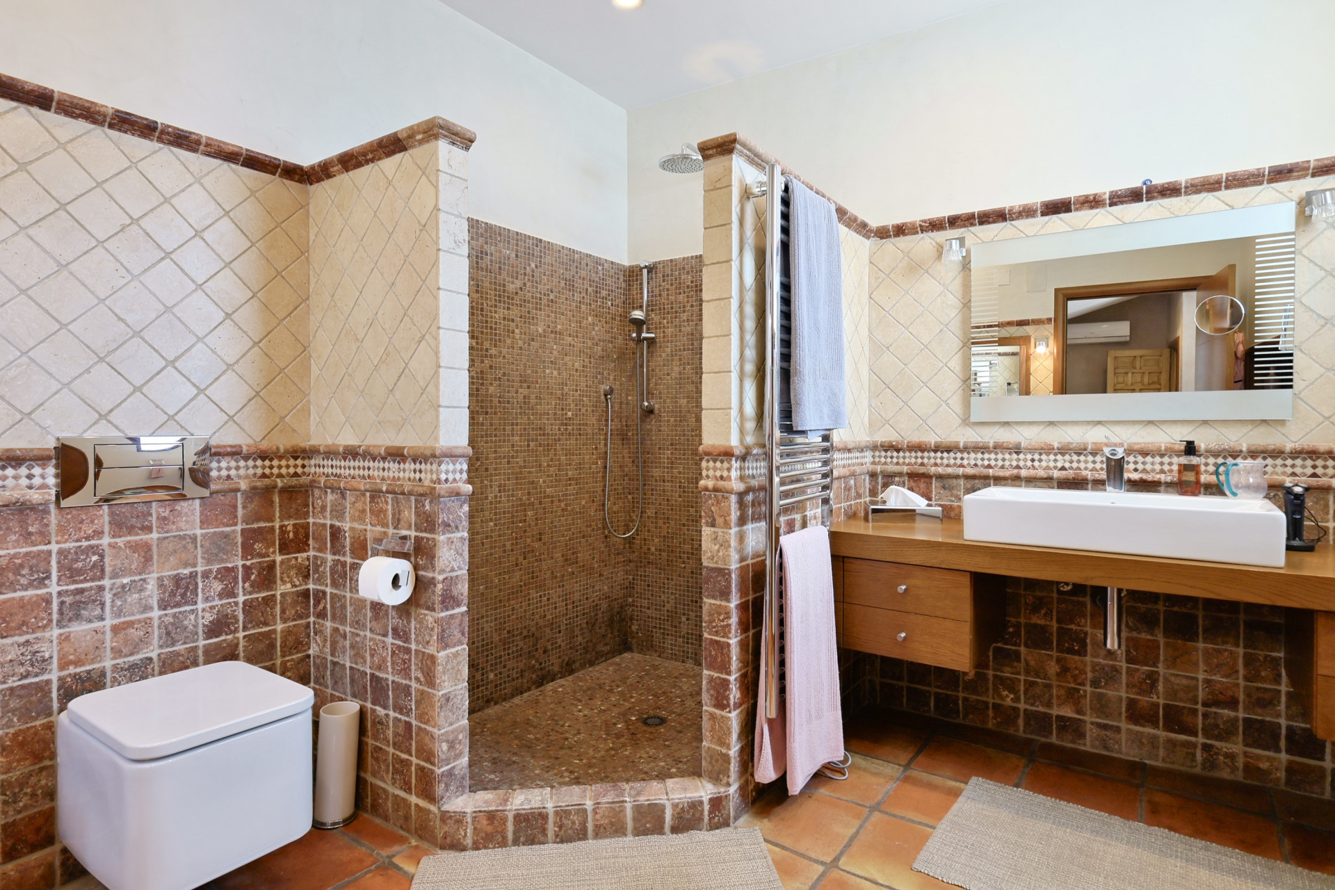 Bathroom detail with mosaic shower, modern sink on wood countertop, and rustic tile.