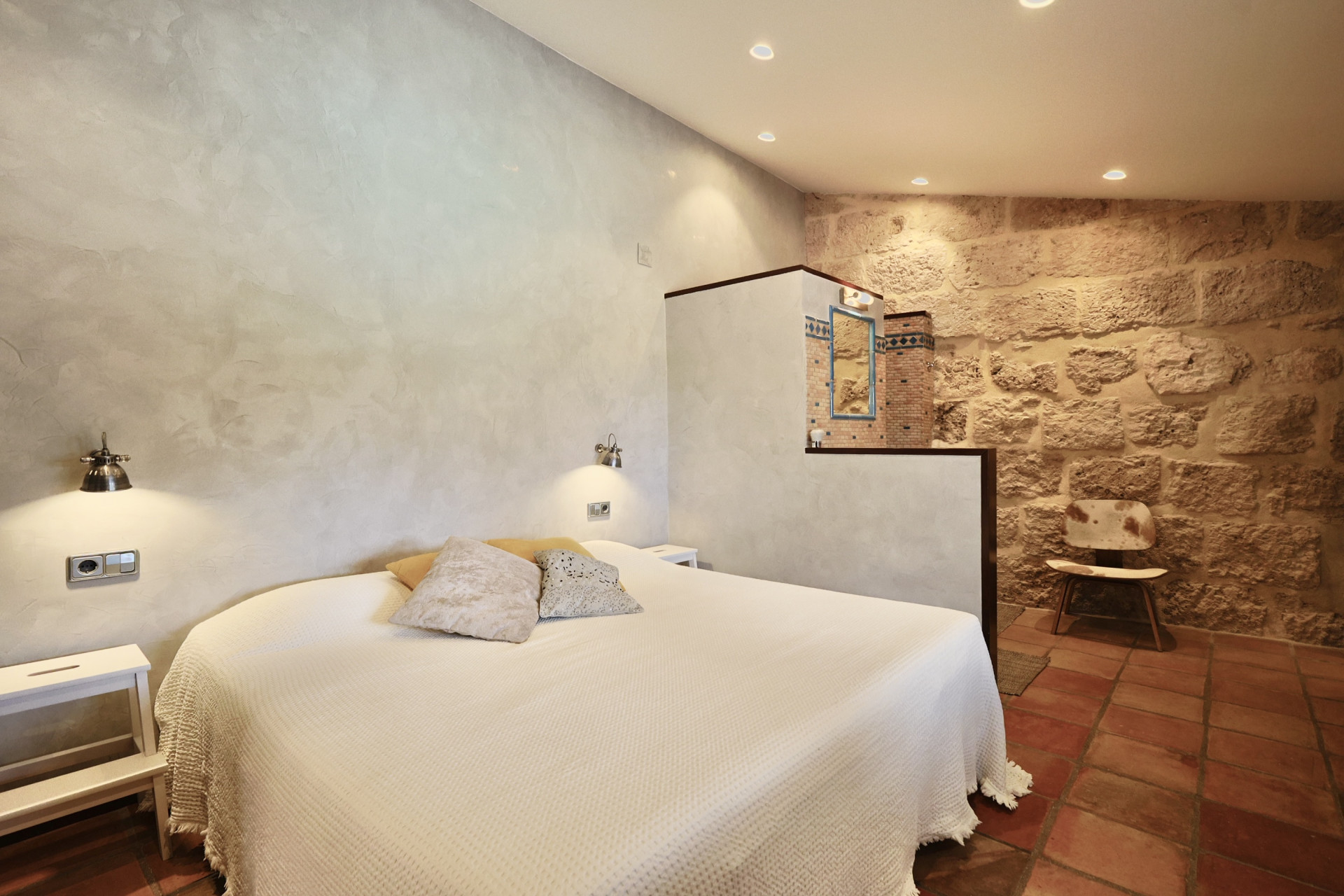 Bedroom featuring an exposed stone wall, double bed with white linens, and terracotta flooring.