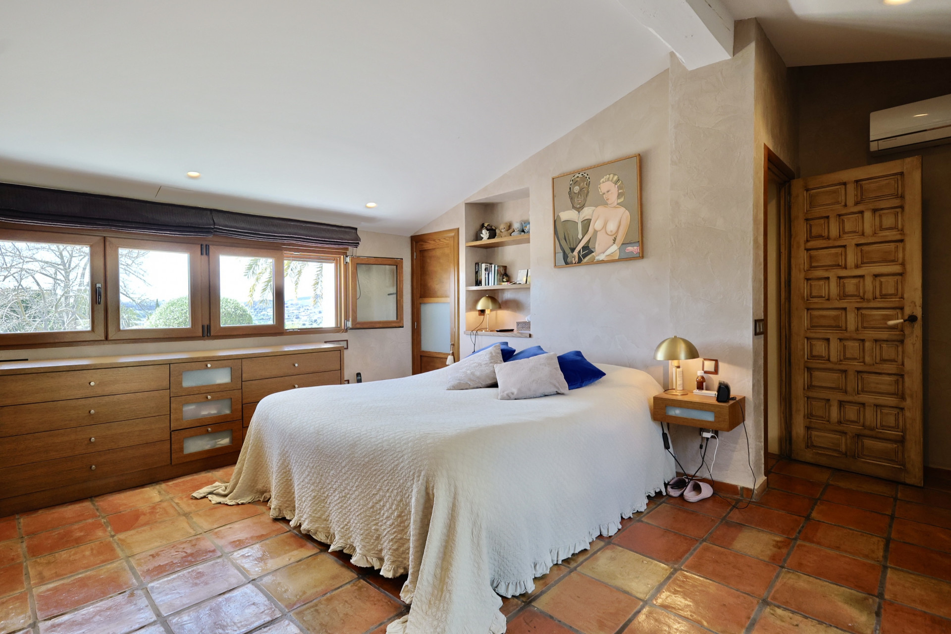 Bedroom featuring terracotta tile flooring, a double bed with white linens, and a wooden headboard with windows.