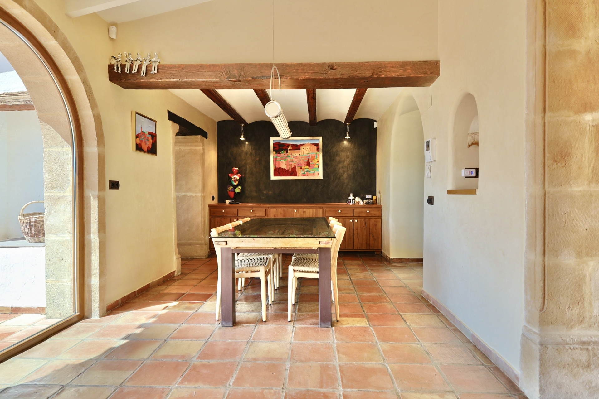 Bright dining room with terracotta floors and wood beams, featuring a glass-topped table.