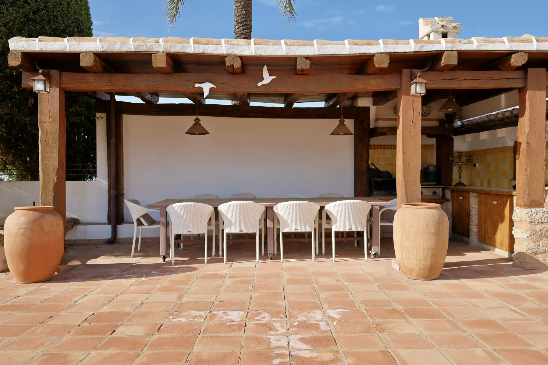 Detail of the covered outdoor terrace with dining table, wicker chairs, and terracotta tile flooring.
