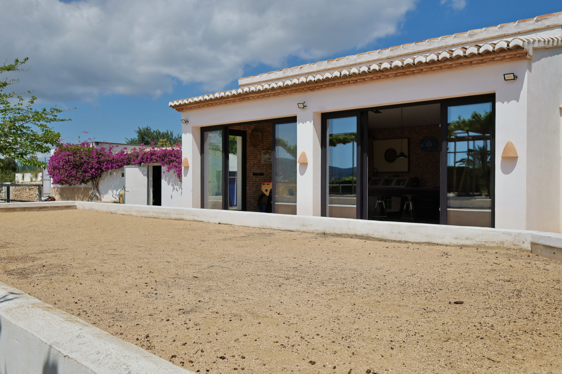 Exterior view of the villa featuring a sand court and large windows reflecting the interior.