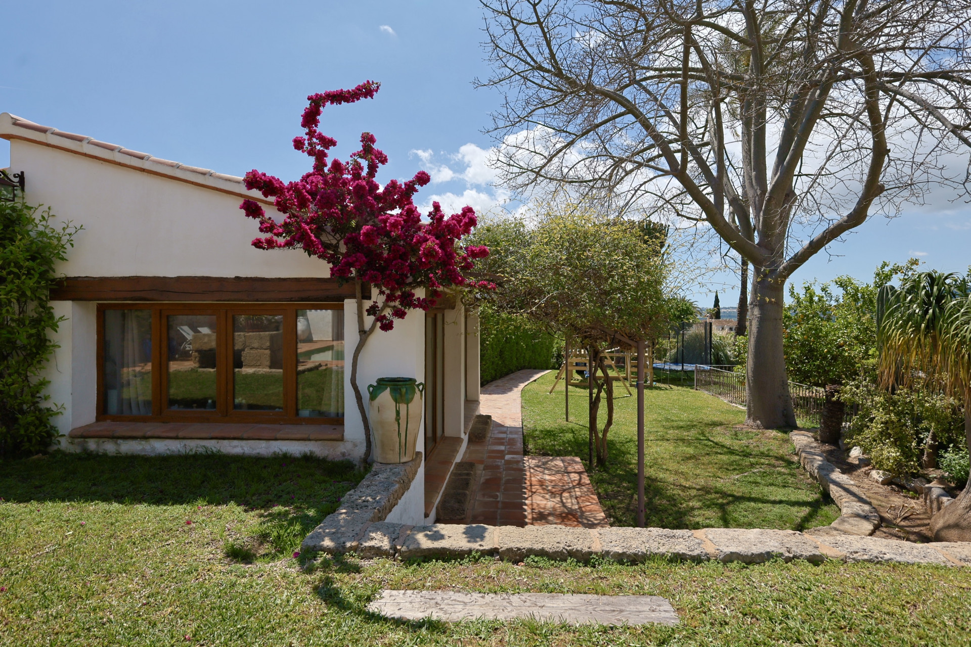 Garden view with fuchsia bougainvillea climbing the facade of the Jávea villa. Window with wooden frame.