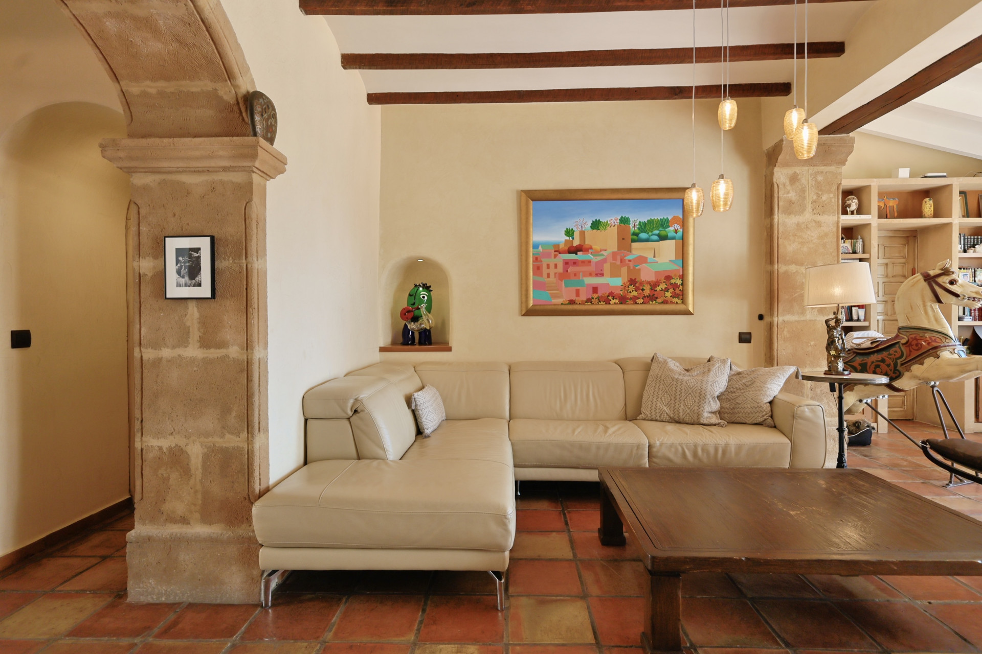 Living room with leather sofa, rustic coffee table, and terracotta flooring. Stone archway detail.