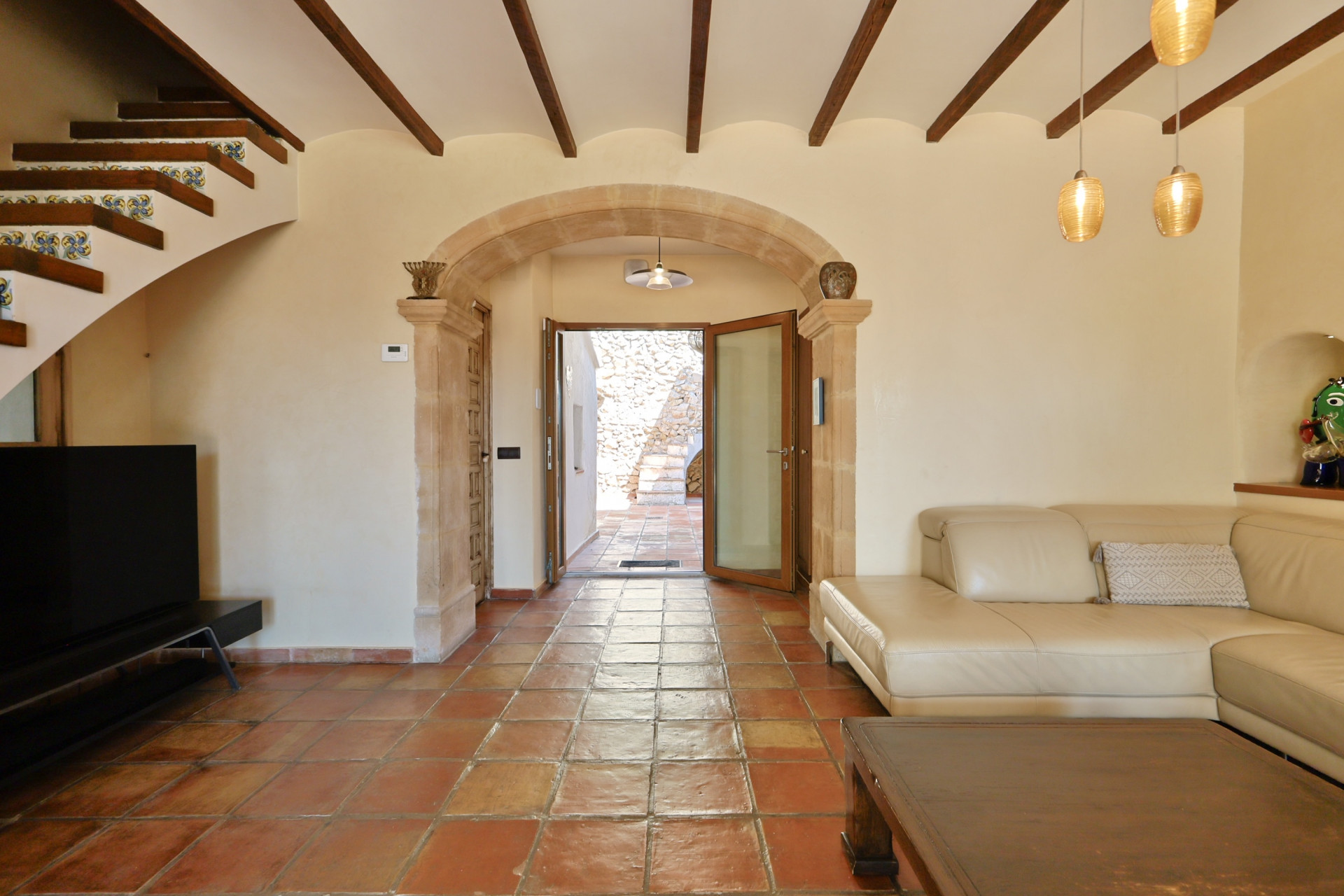 Living room with terracotta floors, leather sofa, and stone archway leading to the outside.