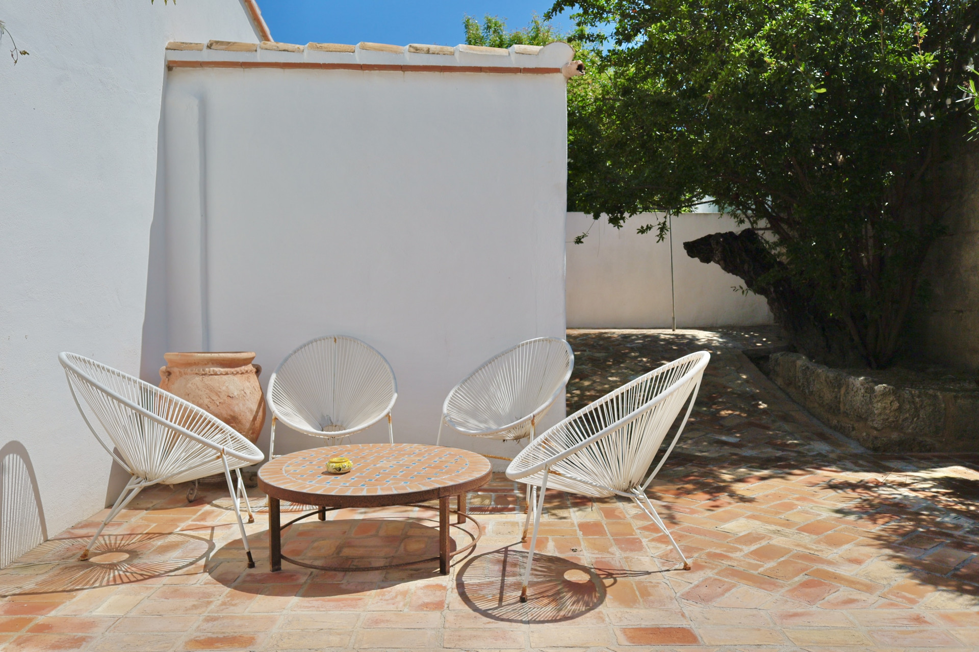 Patio featuring terracotta flooring, white string chairs, and a mosaic table, perfect for outdoor relaxation.