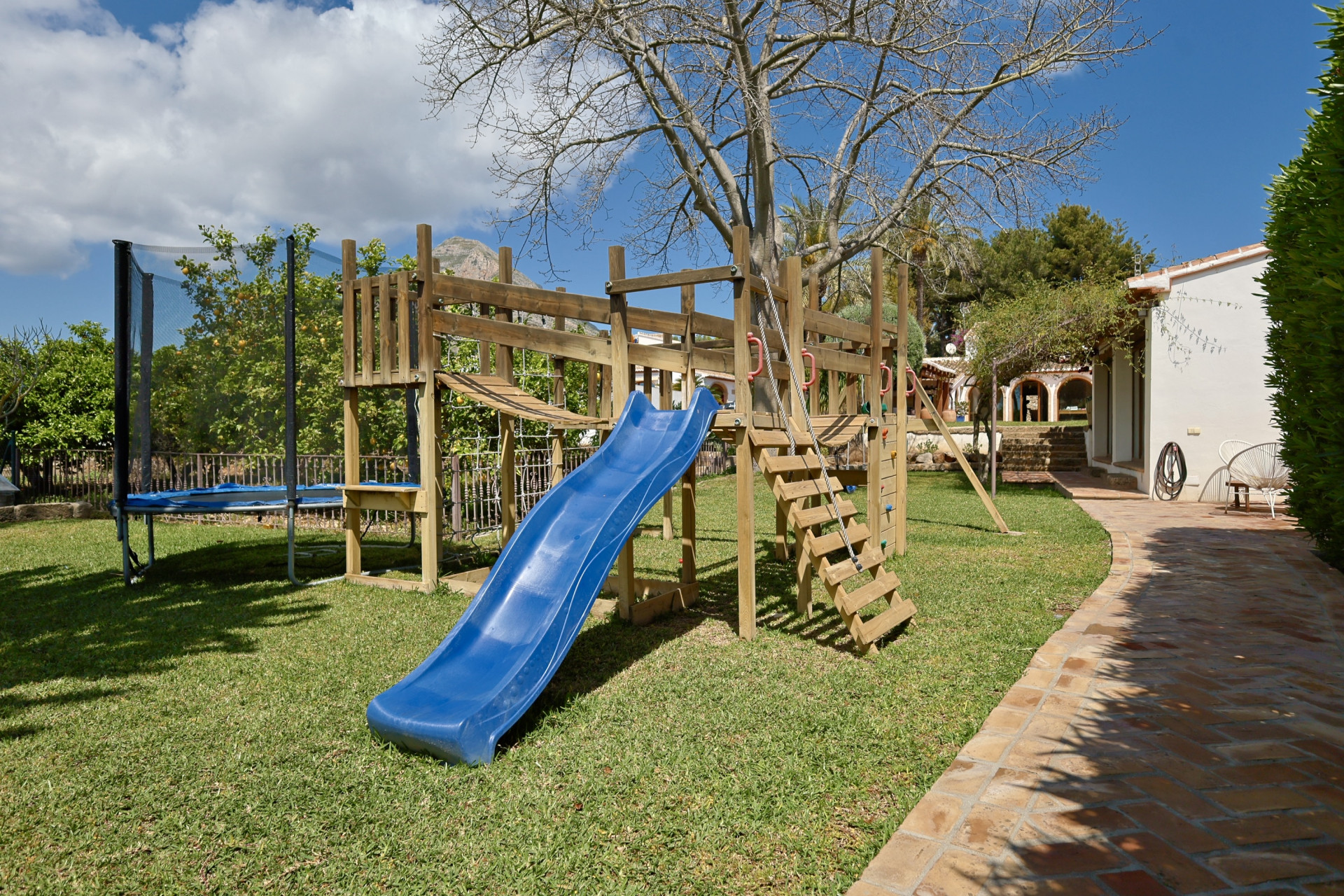 Play area with wooden structure, blue slide, and trampoline in the garden.