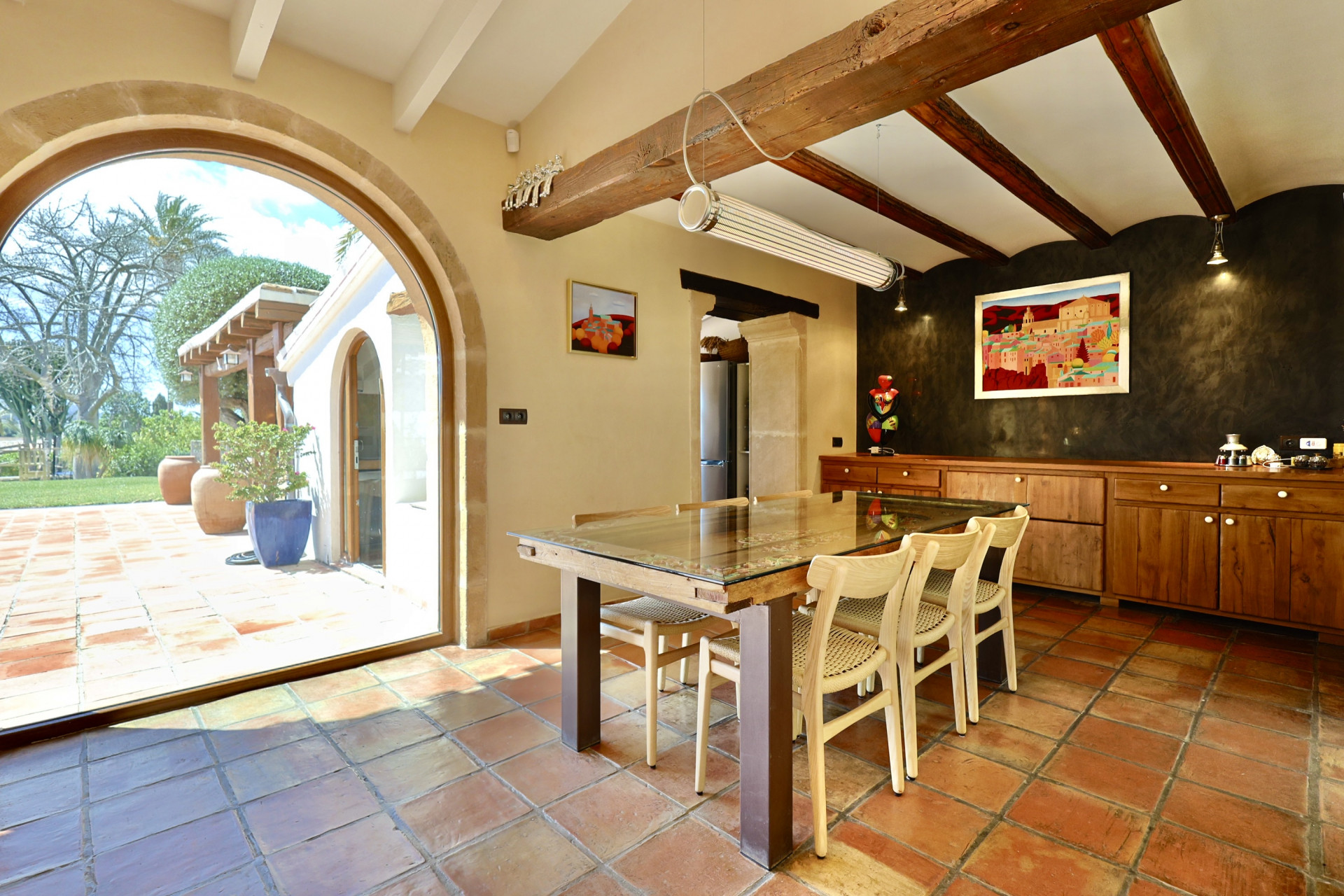 Rustic dining room with terracotta flooring, wood table, and stone archway leading to the garden.
