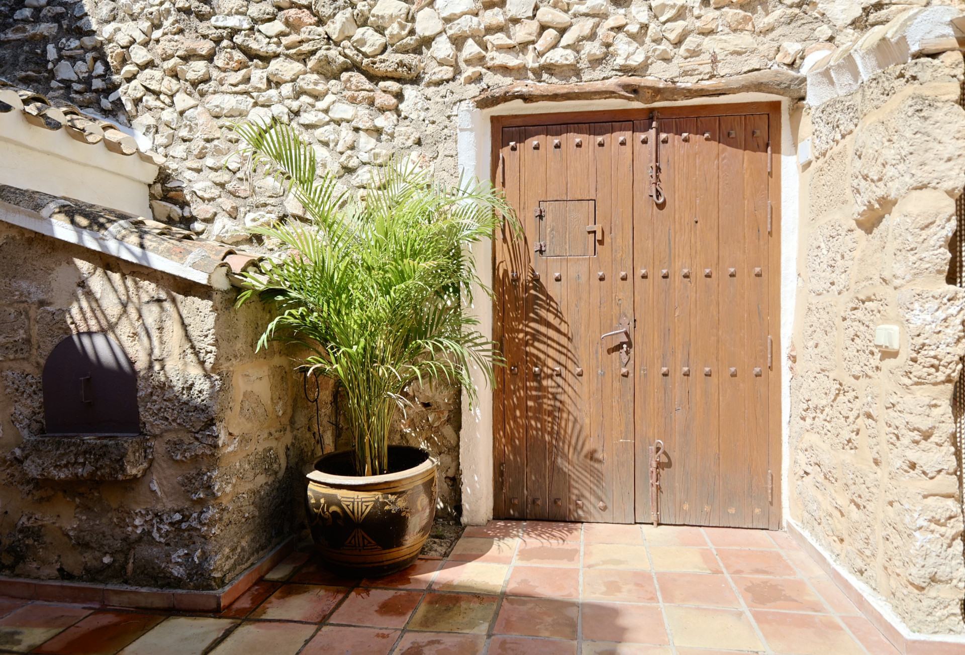 Rustic entrance with studded wooden door and stone wall, next to a potted plant.