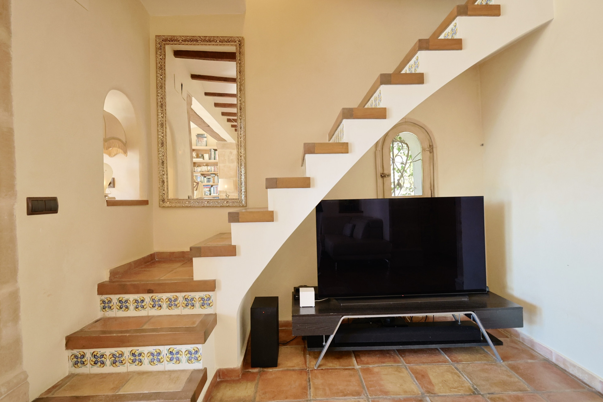 Staircase detail with decorative tiles and TV in living room with terracotta flooring.