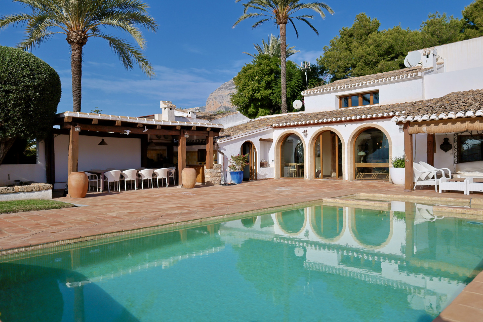 View of the turquoise pool reflecting the arched architecture and pergola with outdoor dining area.