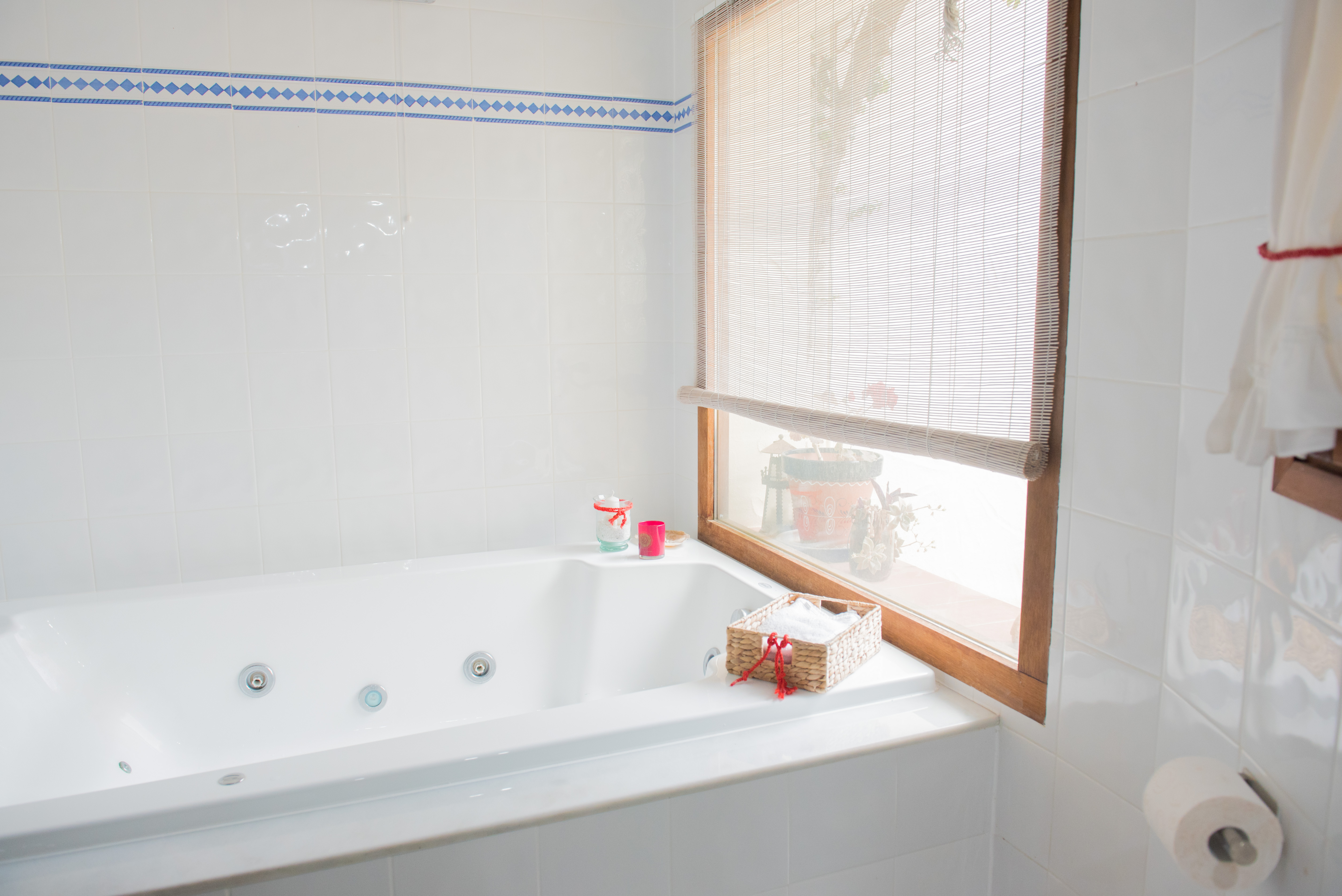 Bathroom featuring a built-in whirlpool bathtub, white wall tiles with a blue border, and a wooden window frame providing soft natural light.