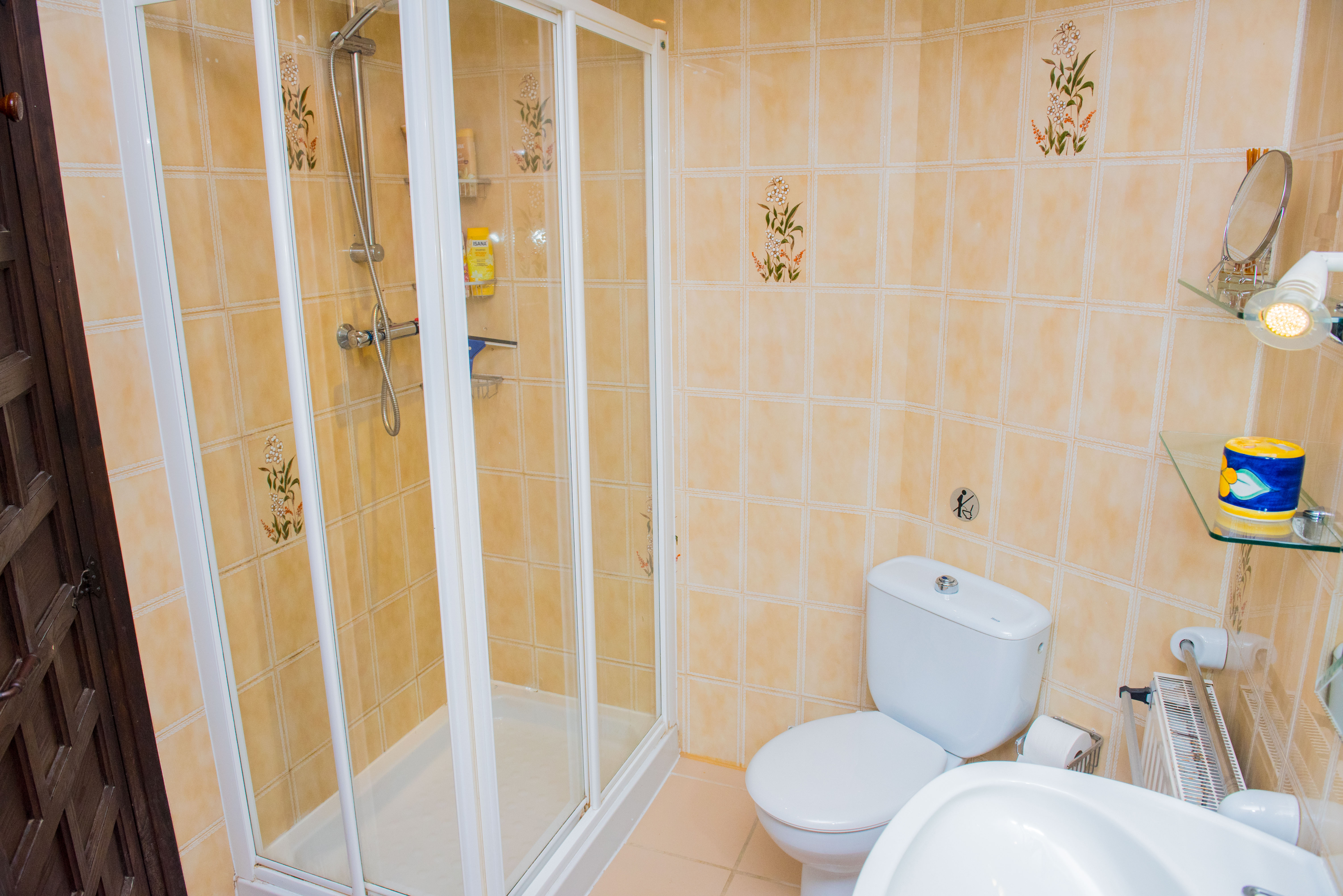 Bathroom featuring a white-framed glass shower enclosure, beige tiled walls with floral accents, and white ceramic sanitary ware.