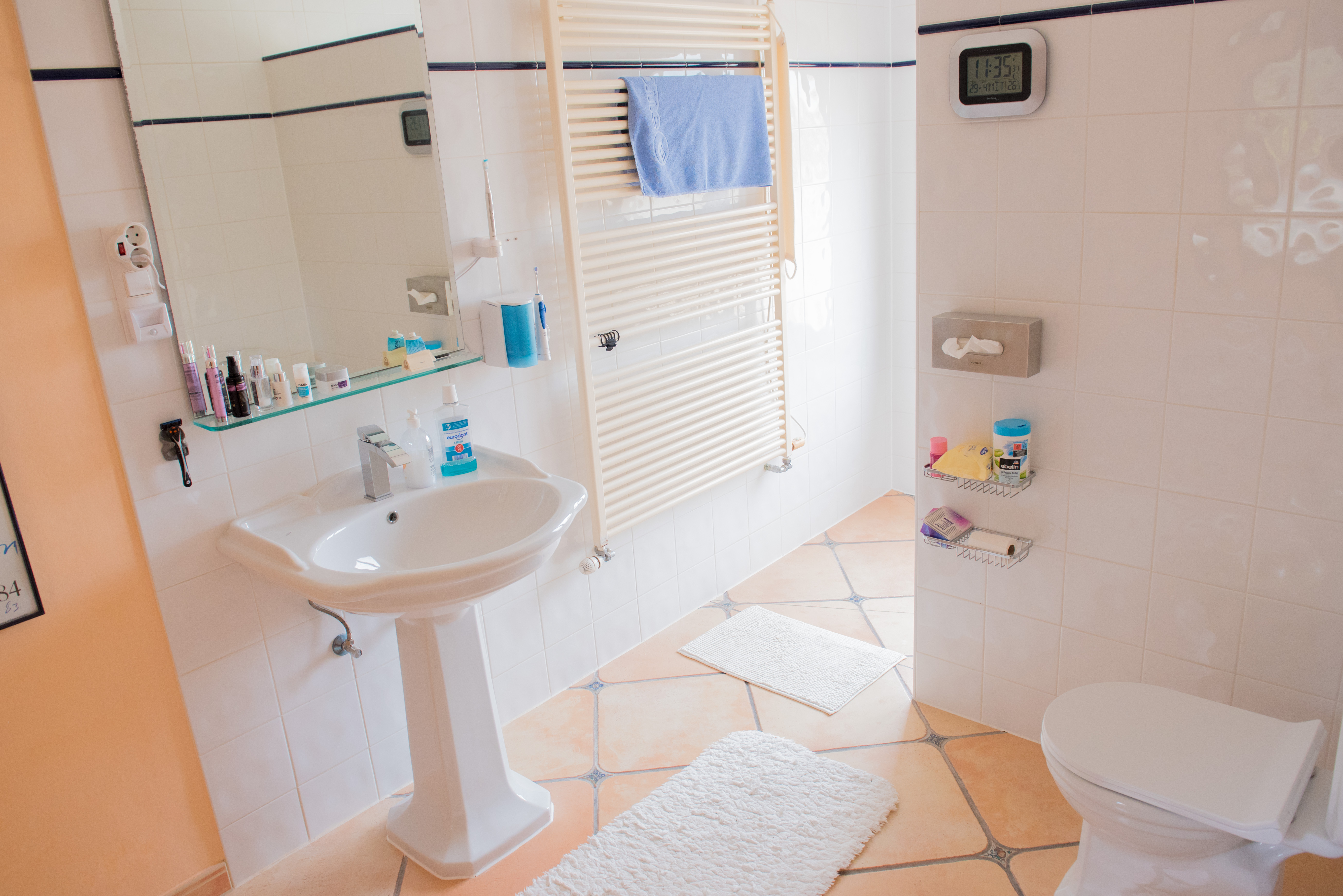 Bathroom featuring a white pedestal sink, terracotta floor tiles with decorative accents, a large heated towel rail, and white wall tiling with a blue border.