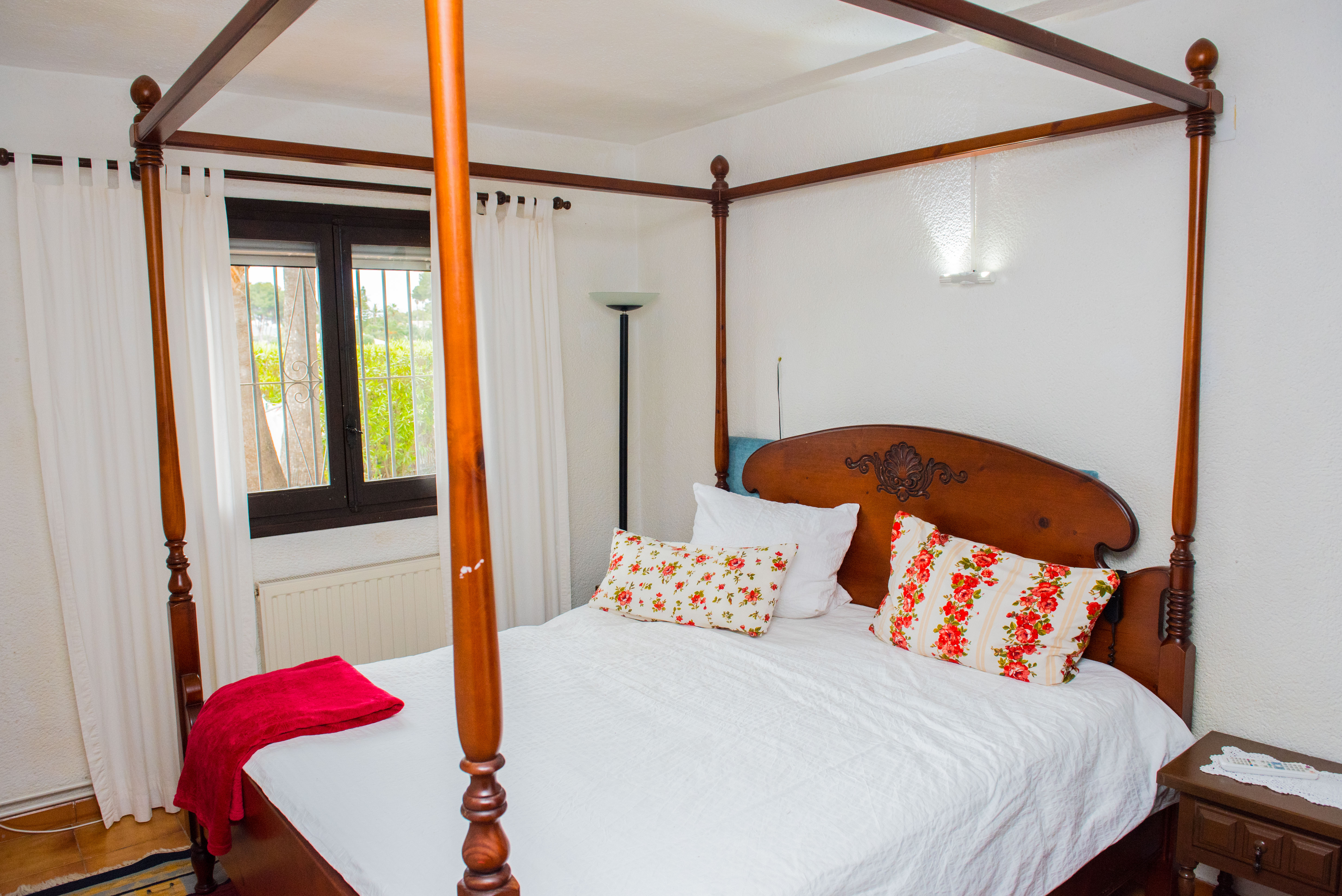 Bedroom featuring a carved wooden four-poster bed, floral patterned pillows, and a window overlooking the garden with integrated radiator heating.