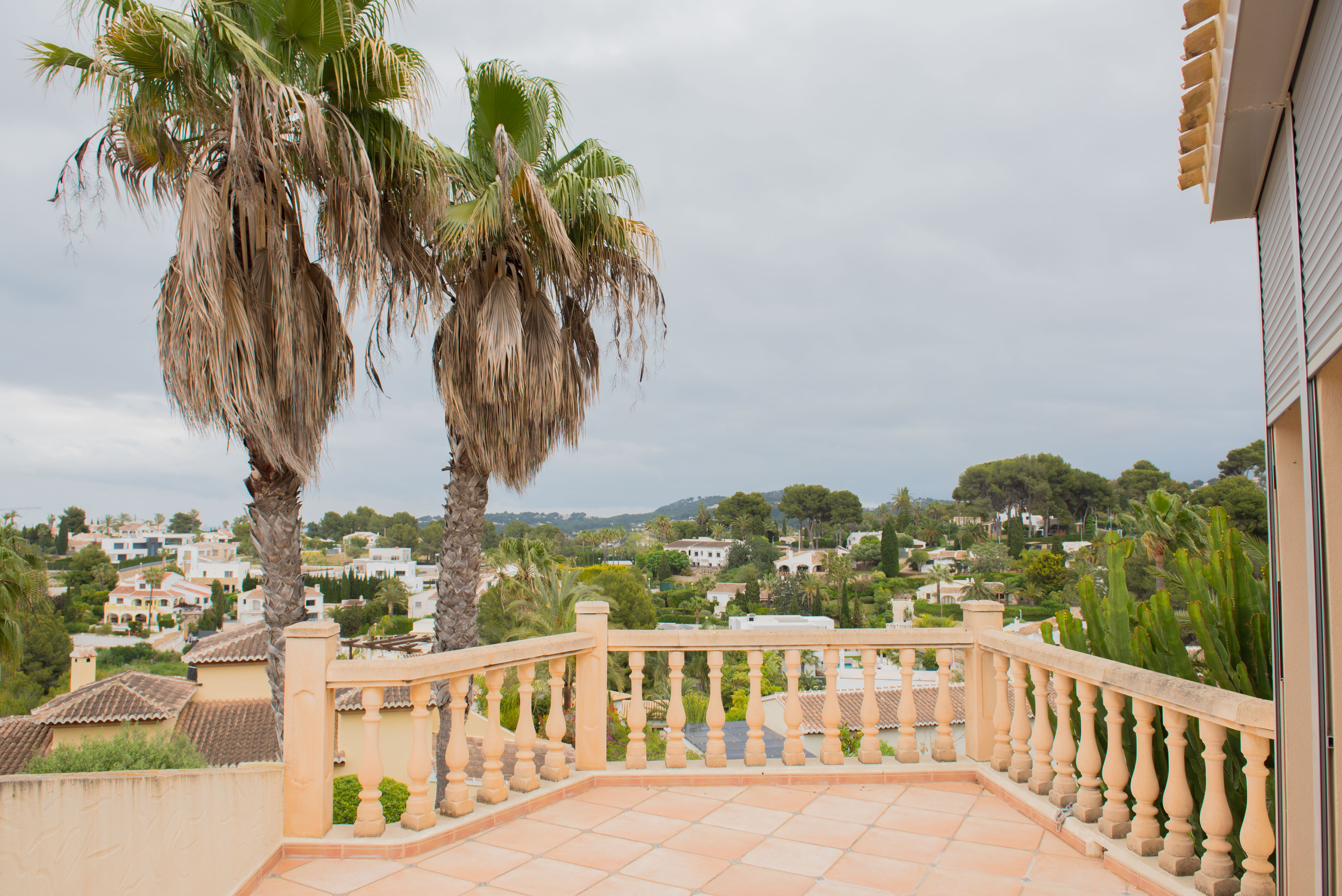 Elevated terrace featuring a classic stone balustrade and terracotta tiling, providing panoramic views of the residential landscape and mature palms.