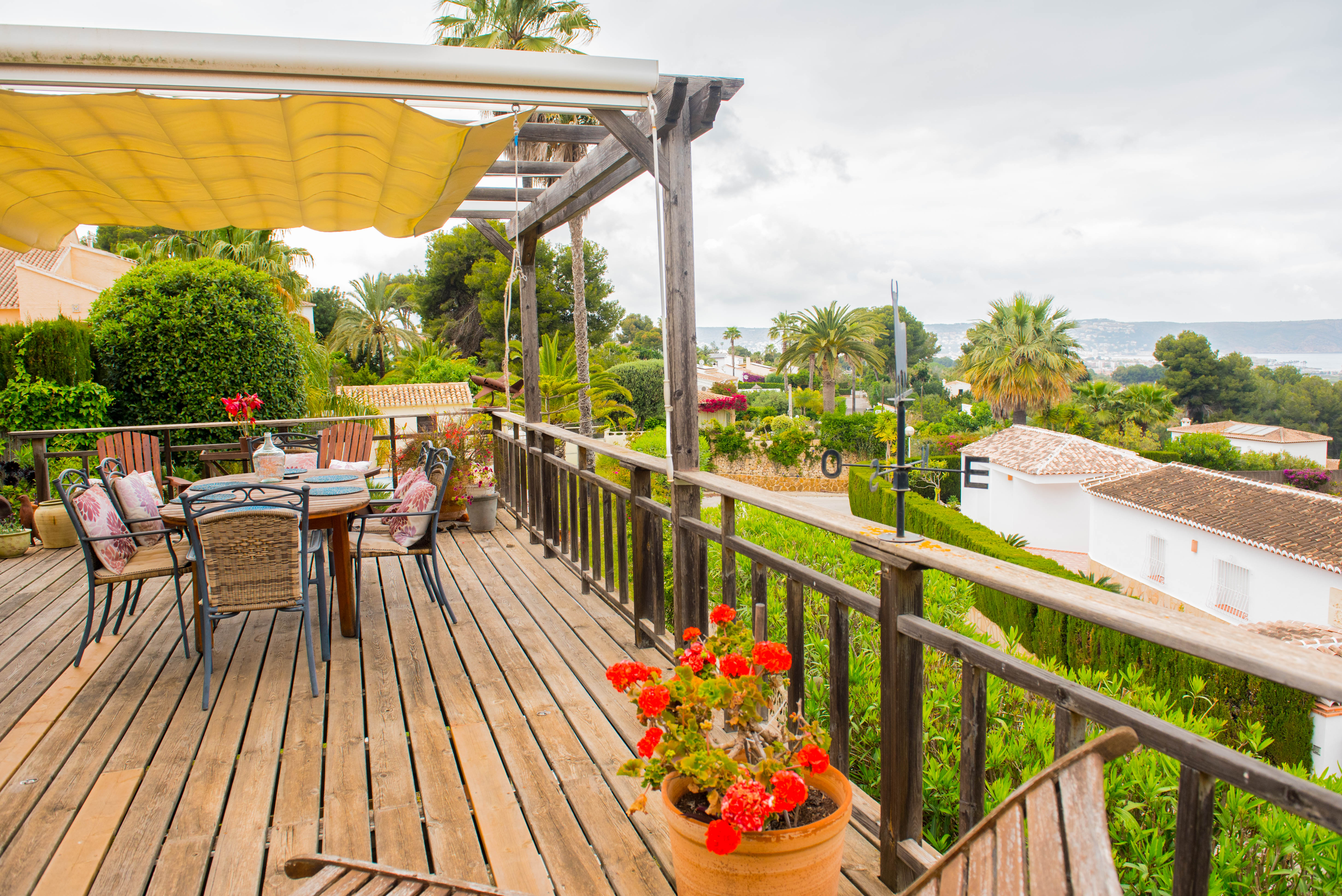 Elevated wooden deck featuring a retractable awning, outdoor dining area, and rustic railings overlooking the Mediterranean landscape and sea.