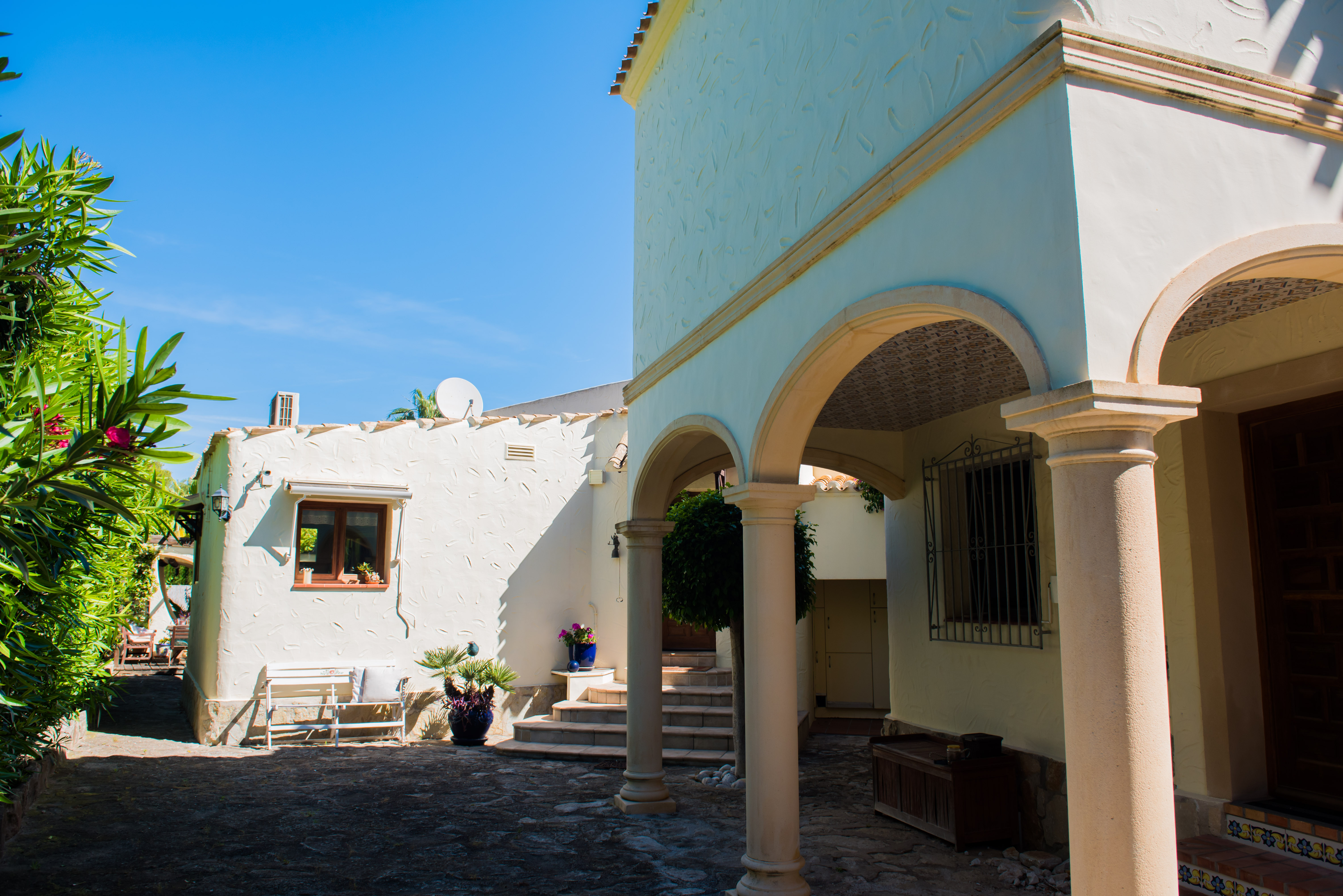 Exterior view of the villa with stone arches and white textured walls, surrounded by Mediterranean greenery. Exterior view of the villa with stone arches and white textured walls, surrounded by Mediterranean greenery.